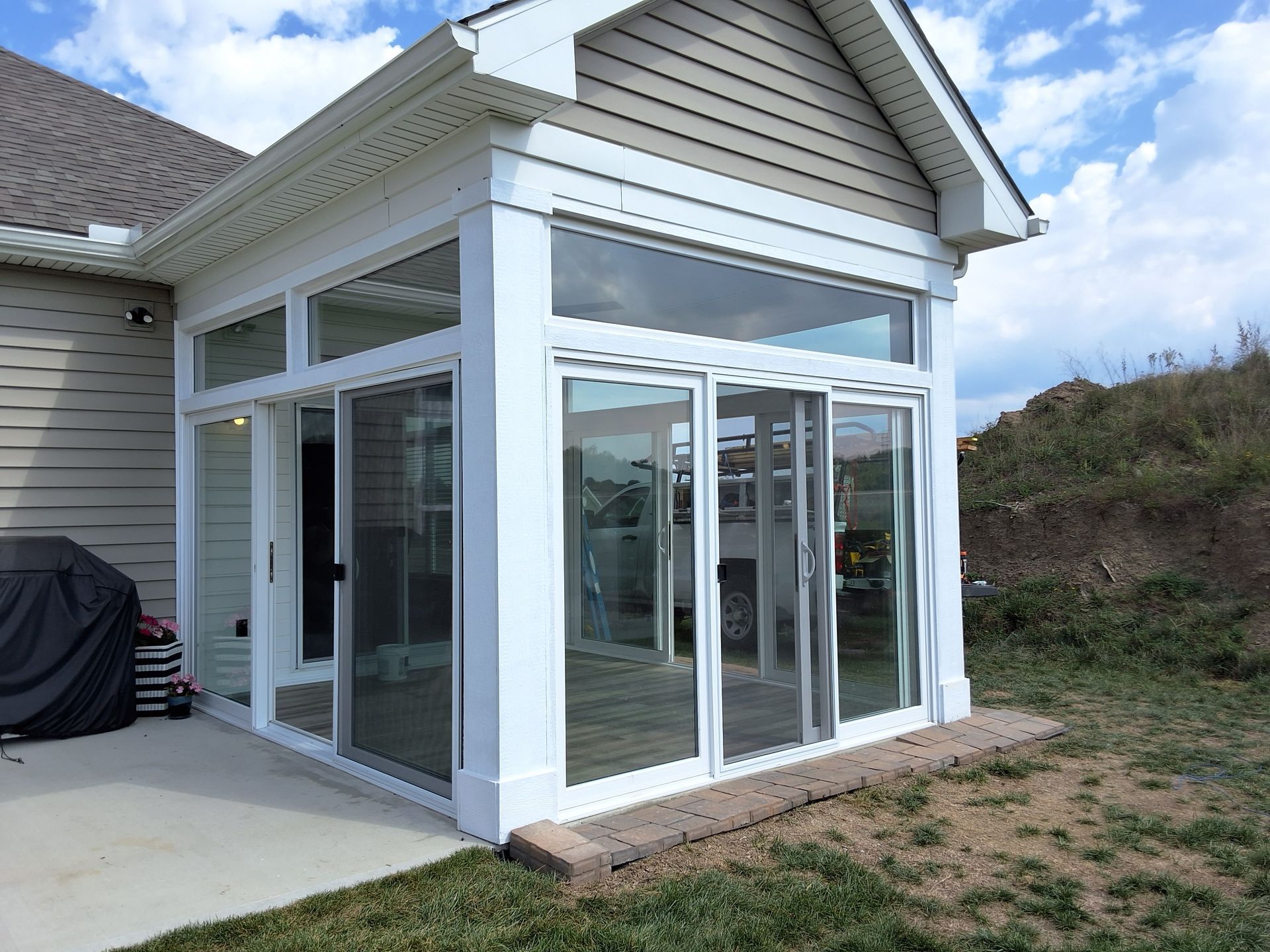 Sunroom addition with glass sliding doors, white trim, and a brick base, attached to a tan house.