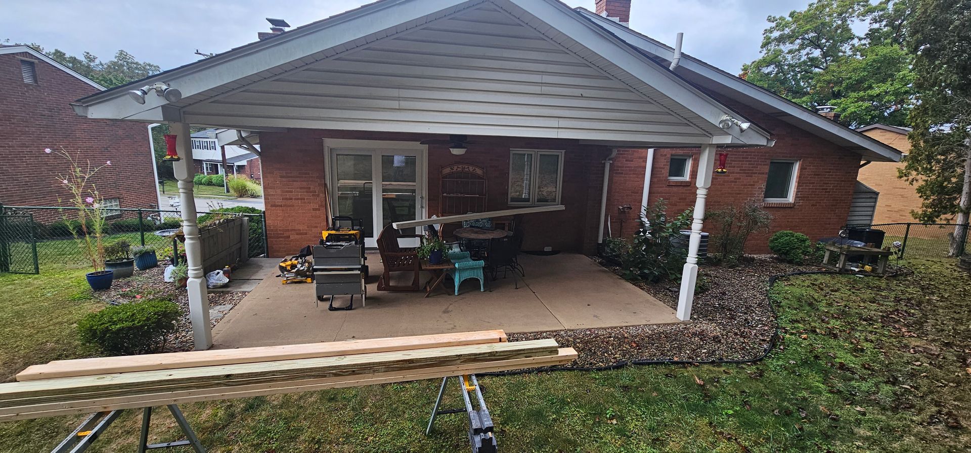 A red brick house with a covered patio, tools, and a lawn.