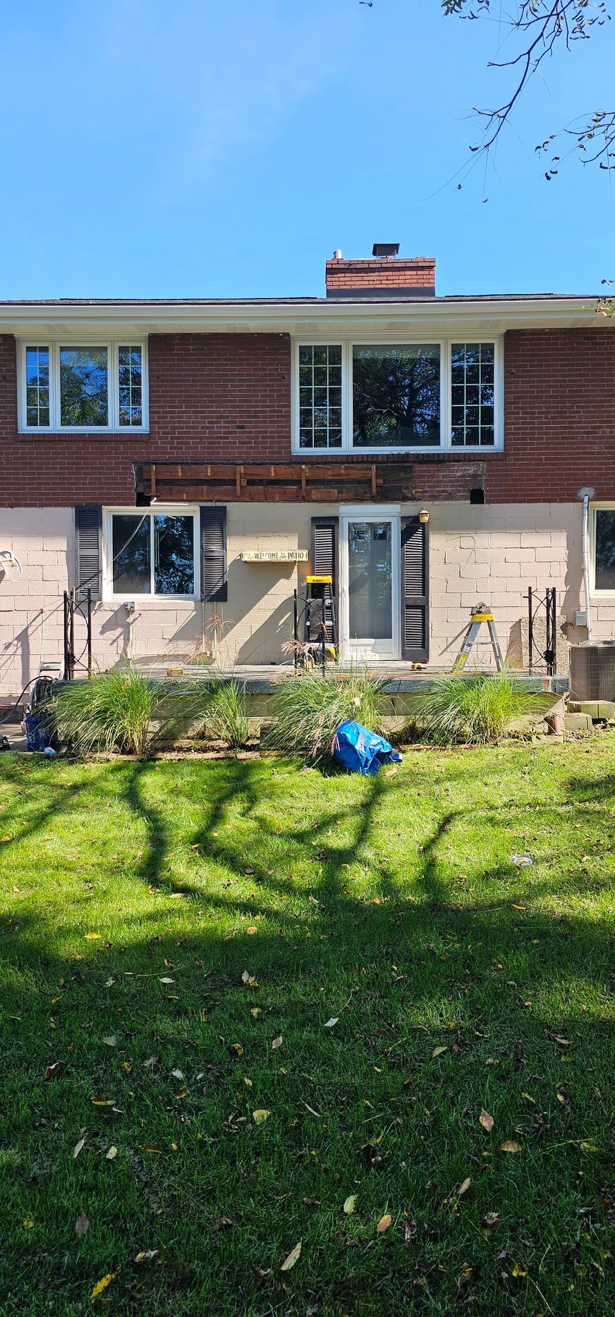 Back of a house with brick and white siding, windows, door, and a grassy yard.
