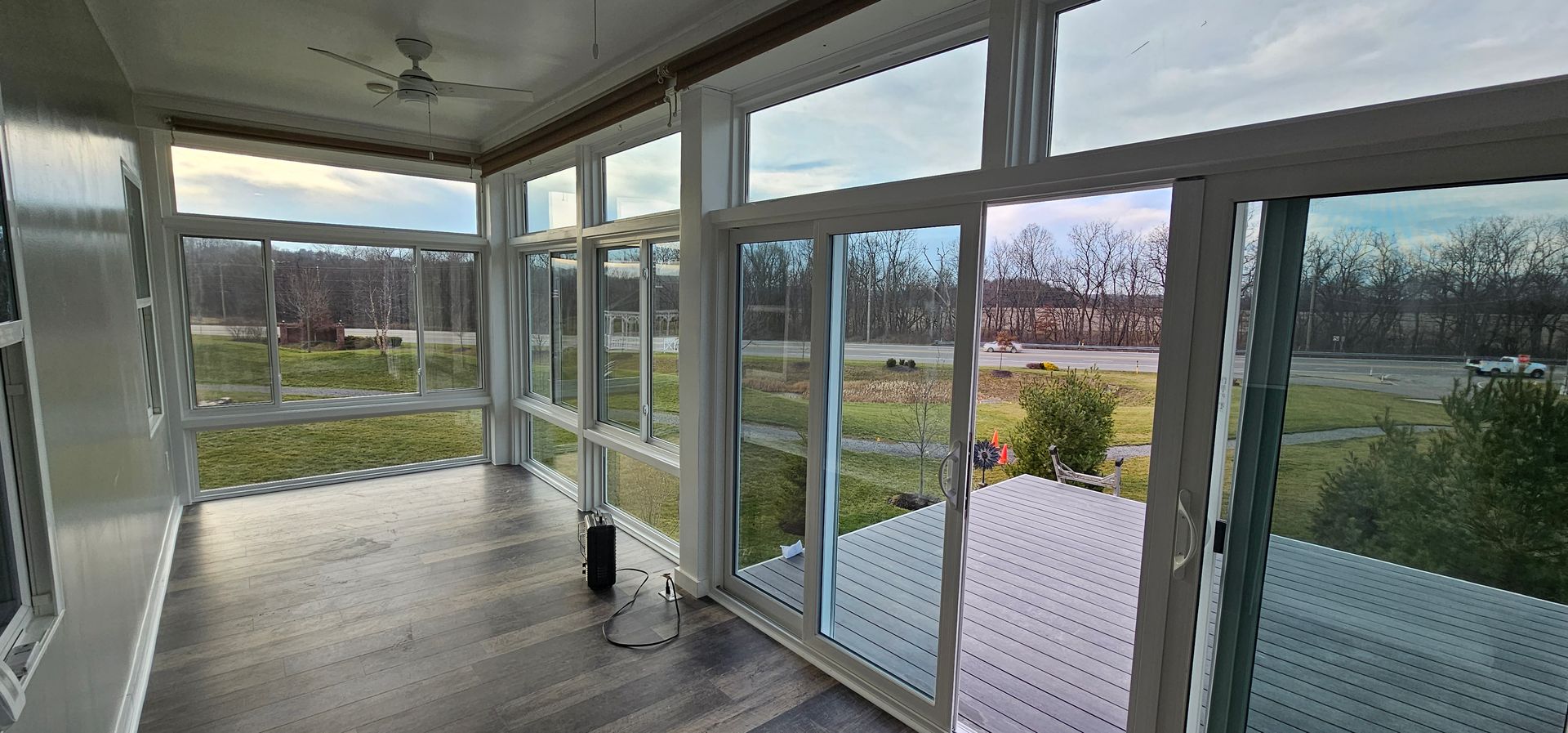 Sunroom with large windows, looking out over a grassy area and trees. Gray floor and white window frames.
