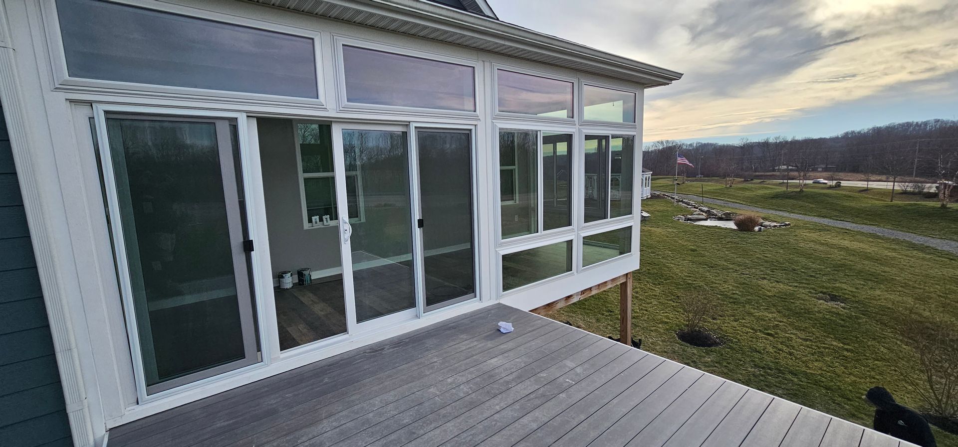 Sunroom with glass windows and door, overlooking a grassy field under a cloudy sky.