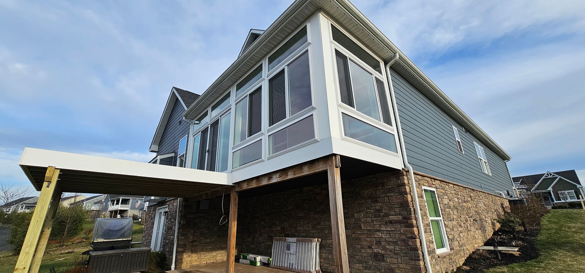 Exterior view of a house with screened porch and a covered deck. Blue siding and stone facade under a cloudy sky.