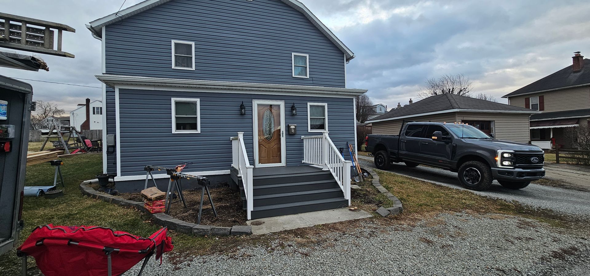 A two-story blue house with white trim. A black truck is parked on the right.