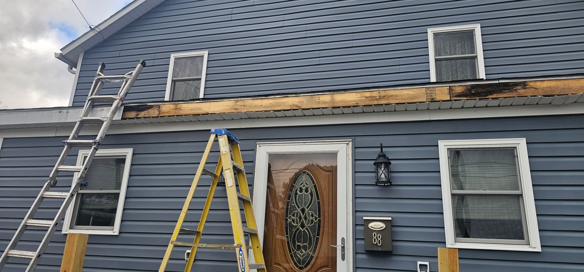 House exterior with ladders propped against the siding and roof. The roof trim appears damaged.