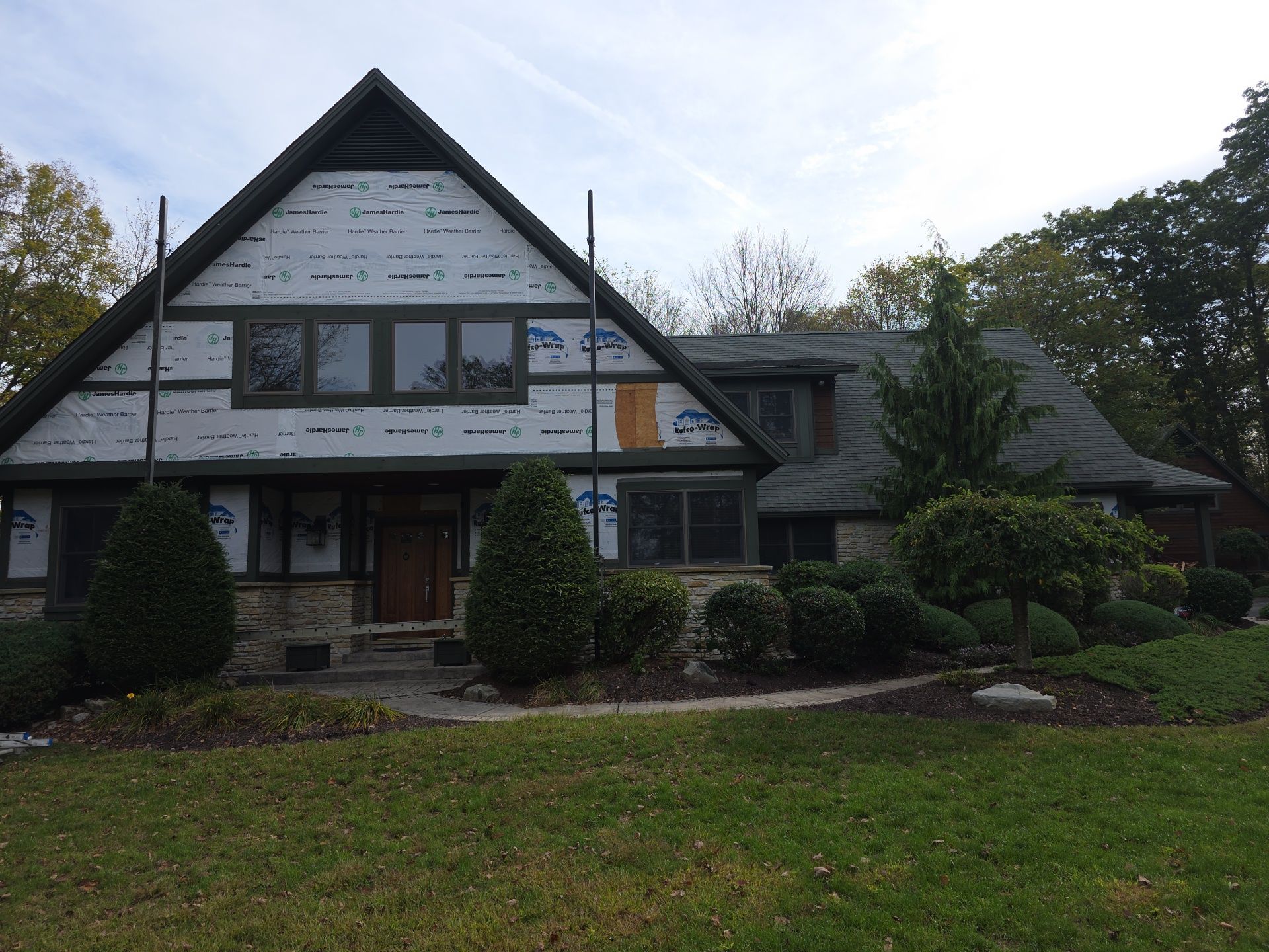 House with exposed siding and brown roof, surrounded by landscaping and a green lawn.