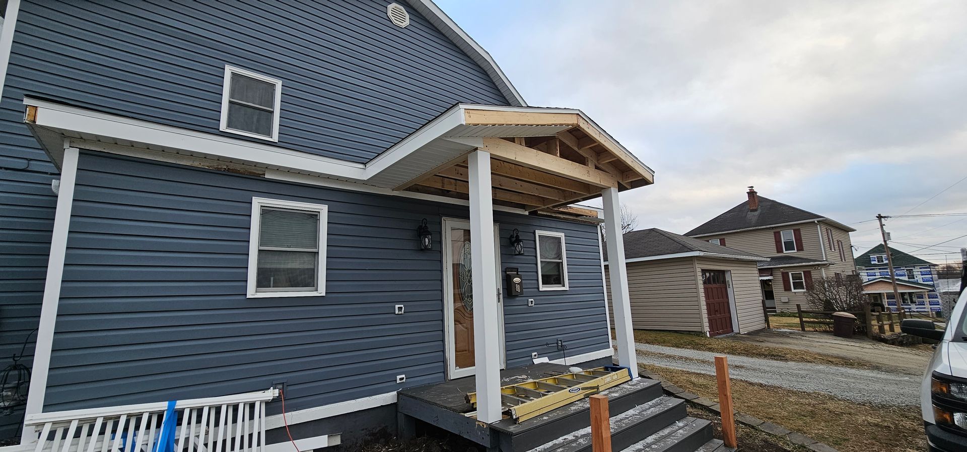 Blue house with a porch under construction, and other buildings in the background. Gray sky.