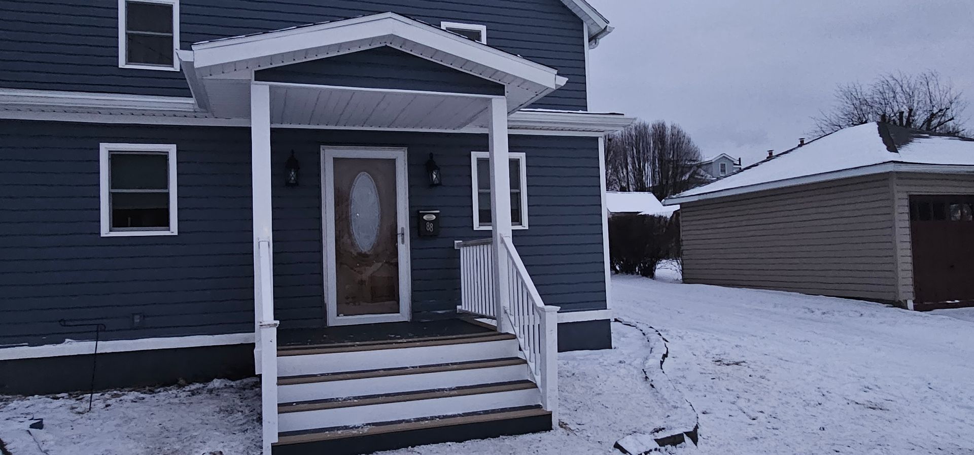 A blue house with a white porch and steps covered in snow. A garage is in the background.