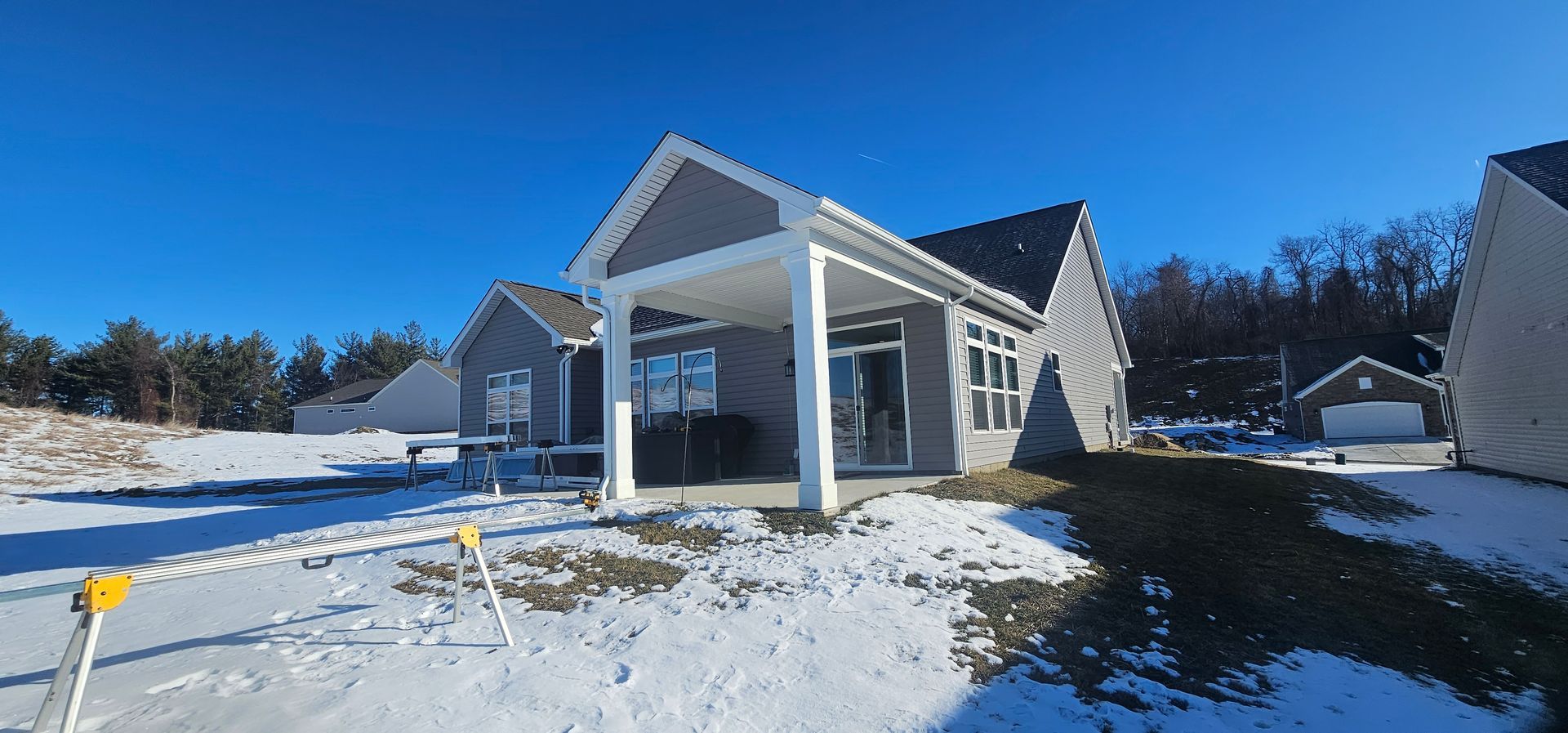 A gray house with a covered porch on a snowy landscape under a bright blue sky.