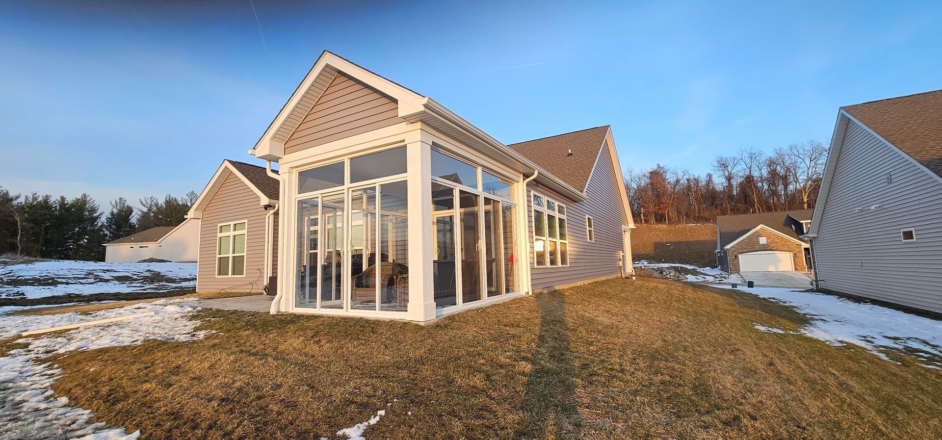 A home with a glass sunroom, set in a yard with patches of snow and dry grass.
