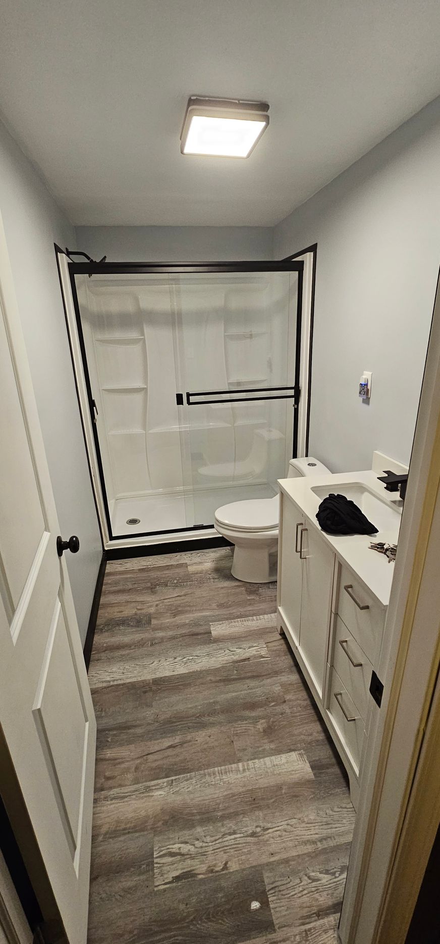 Bathroom with a shower, toilet, and vanity. The floors are wood-like with gray walls.