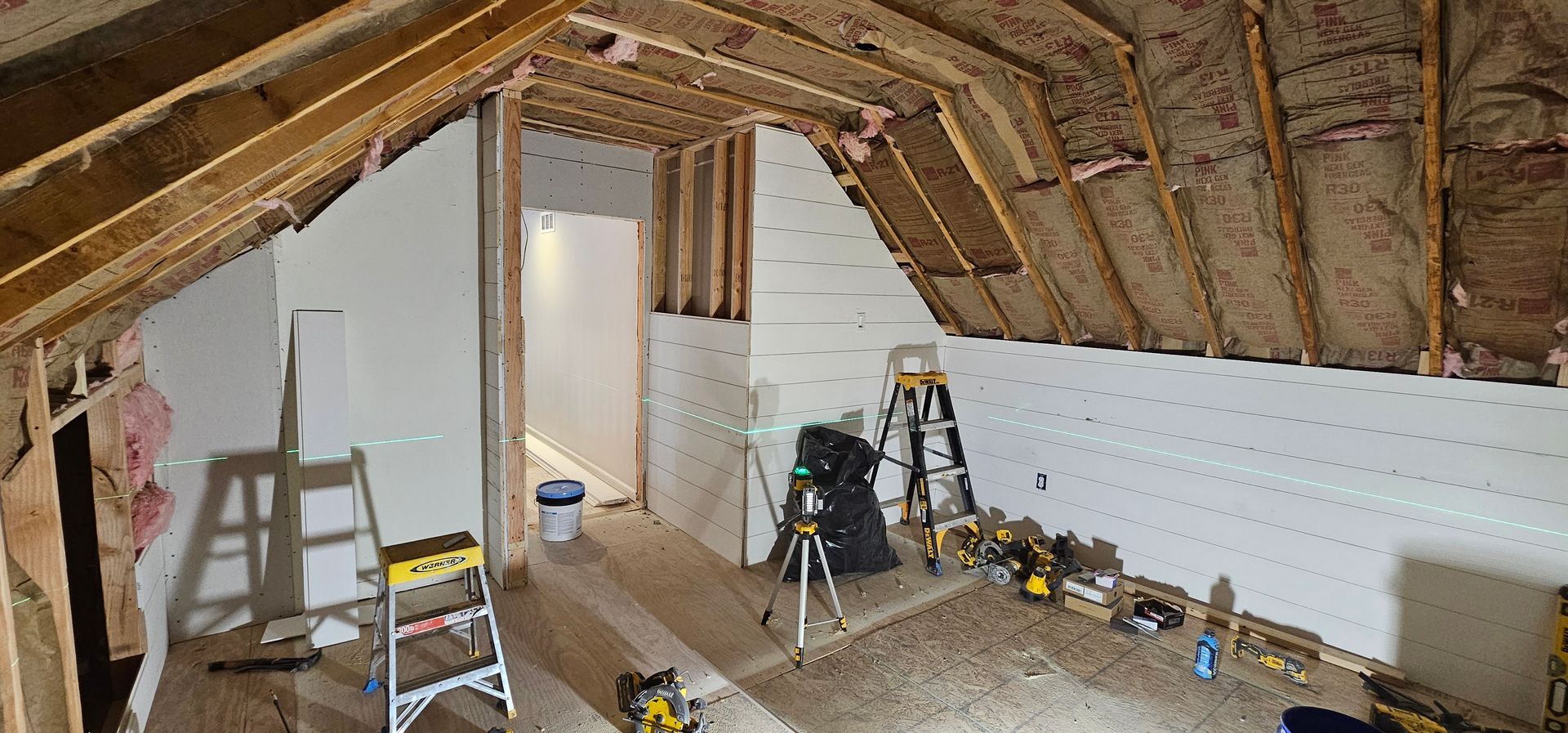 Interior of an attic under construction with exposed beams, drywall, and tools scattered about.