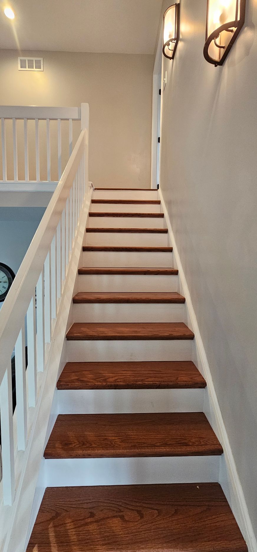Wooden staircase with white banister, leading upwards to a door. Two sconces on the wall.