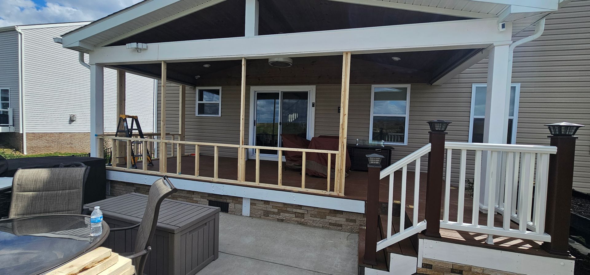 Back porch with unfinished railing. Brown wood and beige siding on a sunny day.