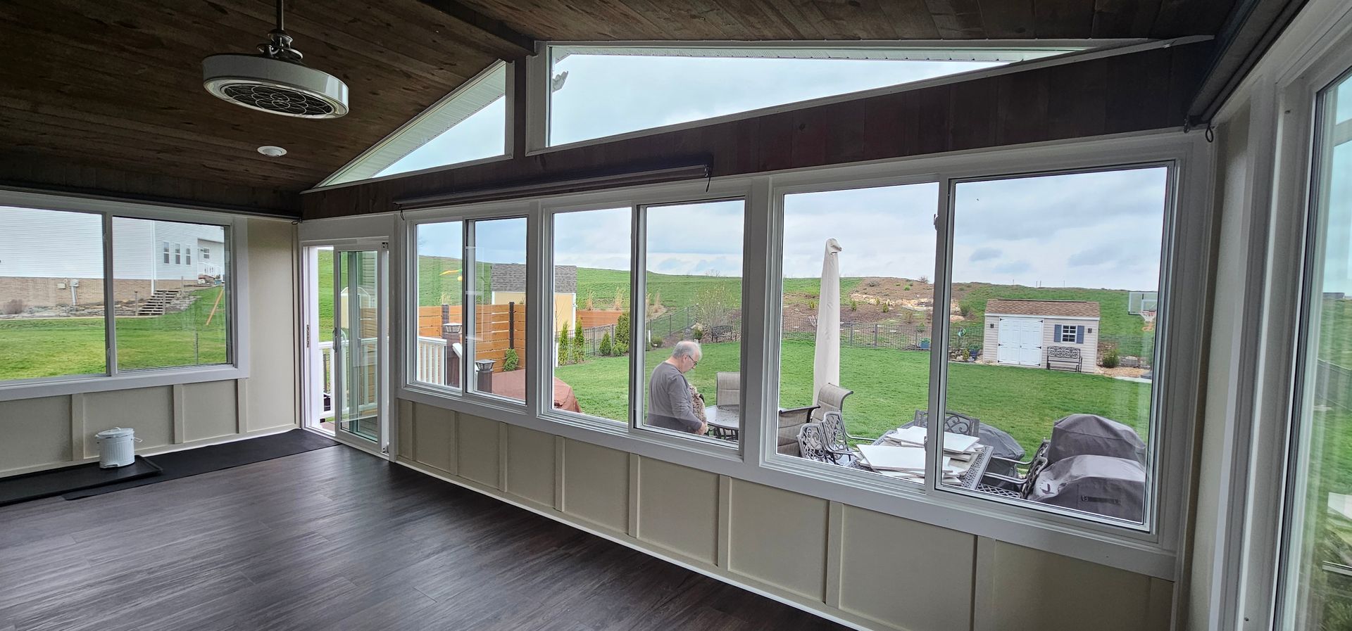 Sunroom with dark wood floor and ceiling, white trim, and a view of green grass and the sky.