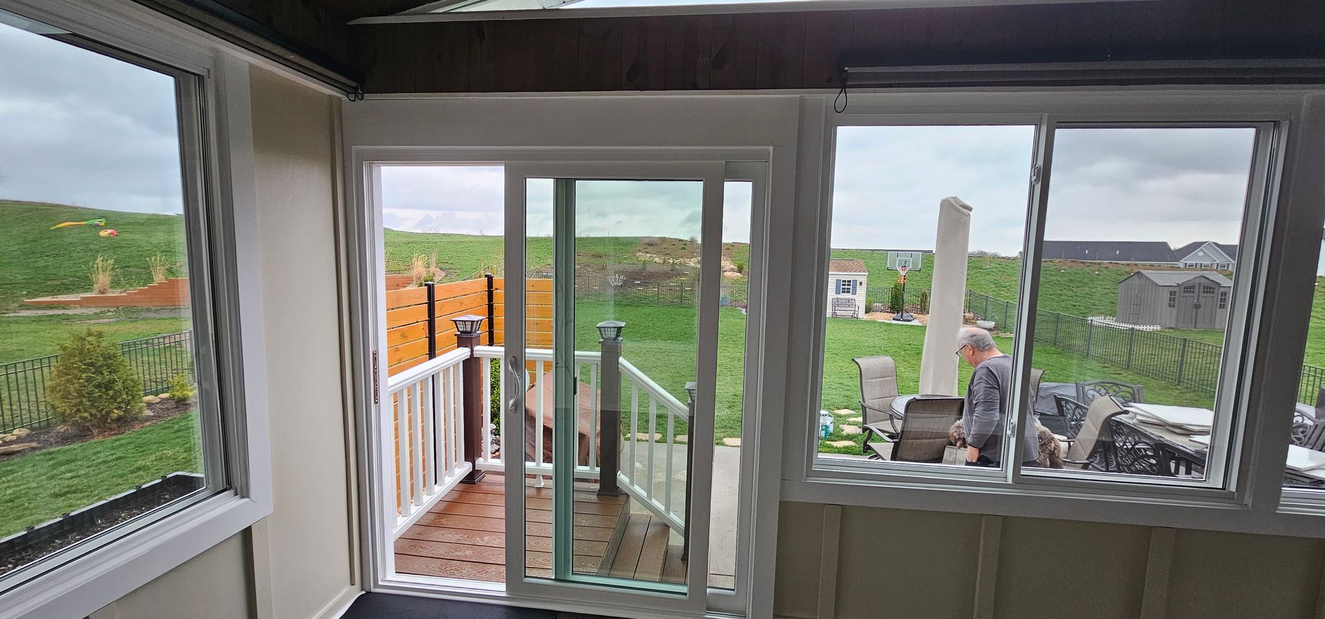 Sunroom with windows overlooking a backyard and a person outside, cloudy day.