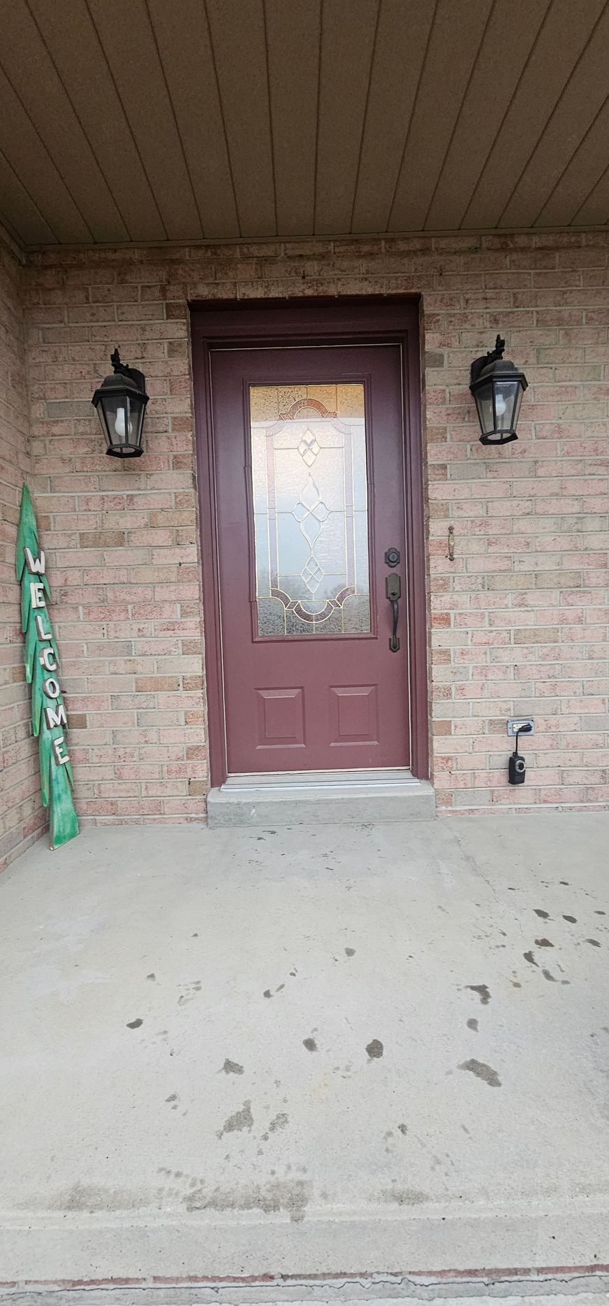 A maroon door with glass and side lamps, set in a brick wall porch.