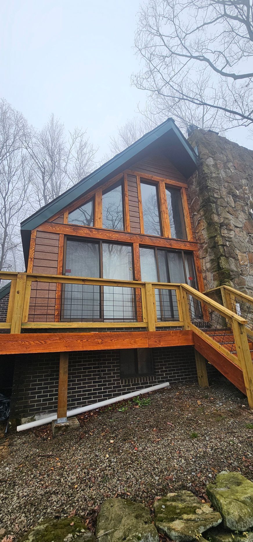 Cabin with large windows and a stone chimney, surrounded by trees.