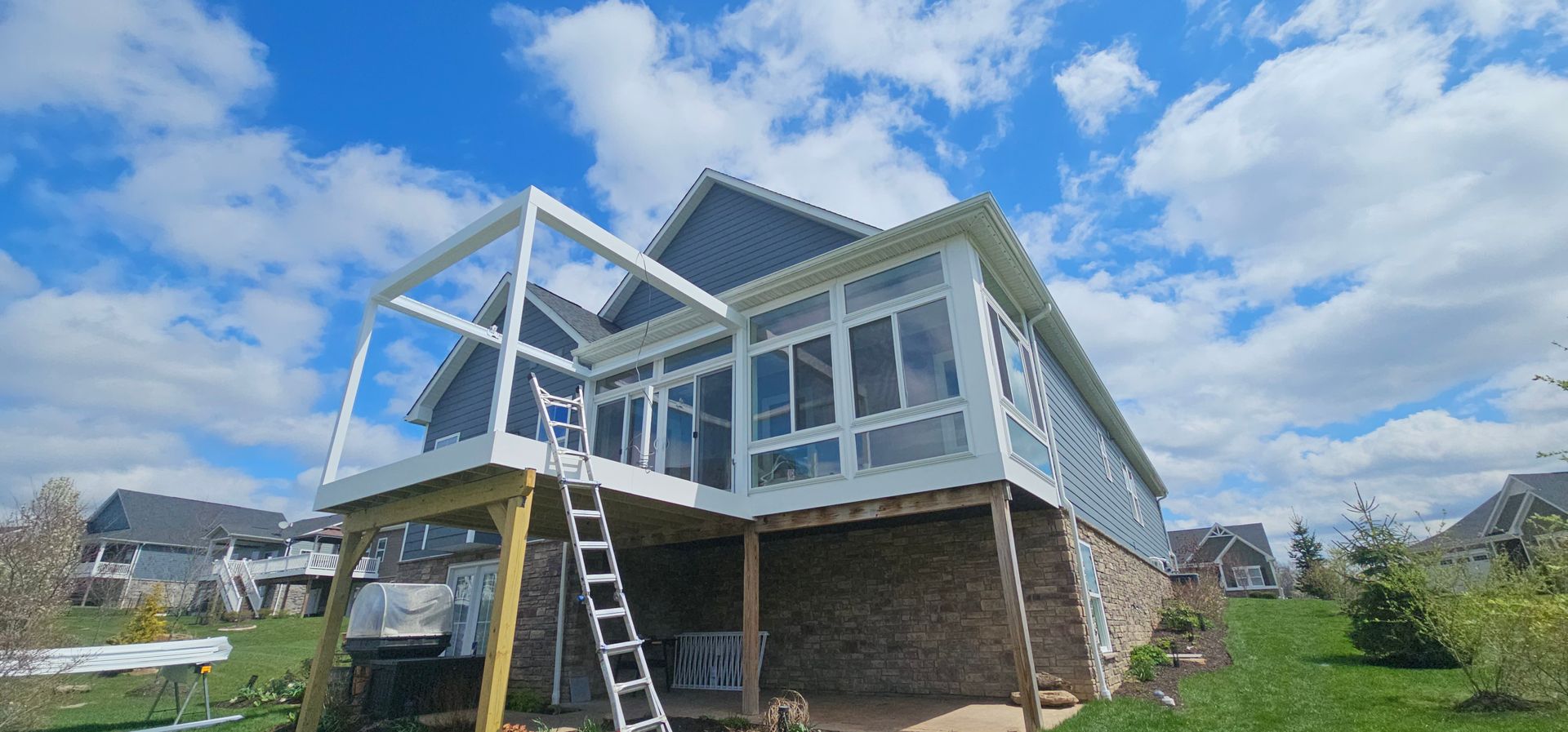 A house with a screened-in porch and deck, brick facade, blue sky, and green grass.