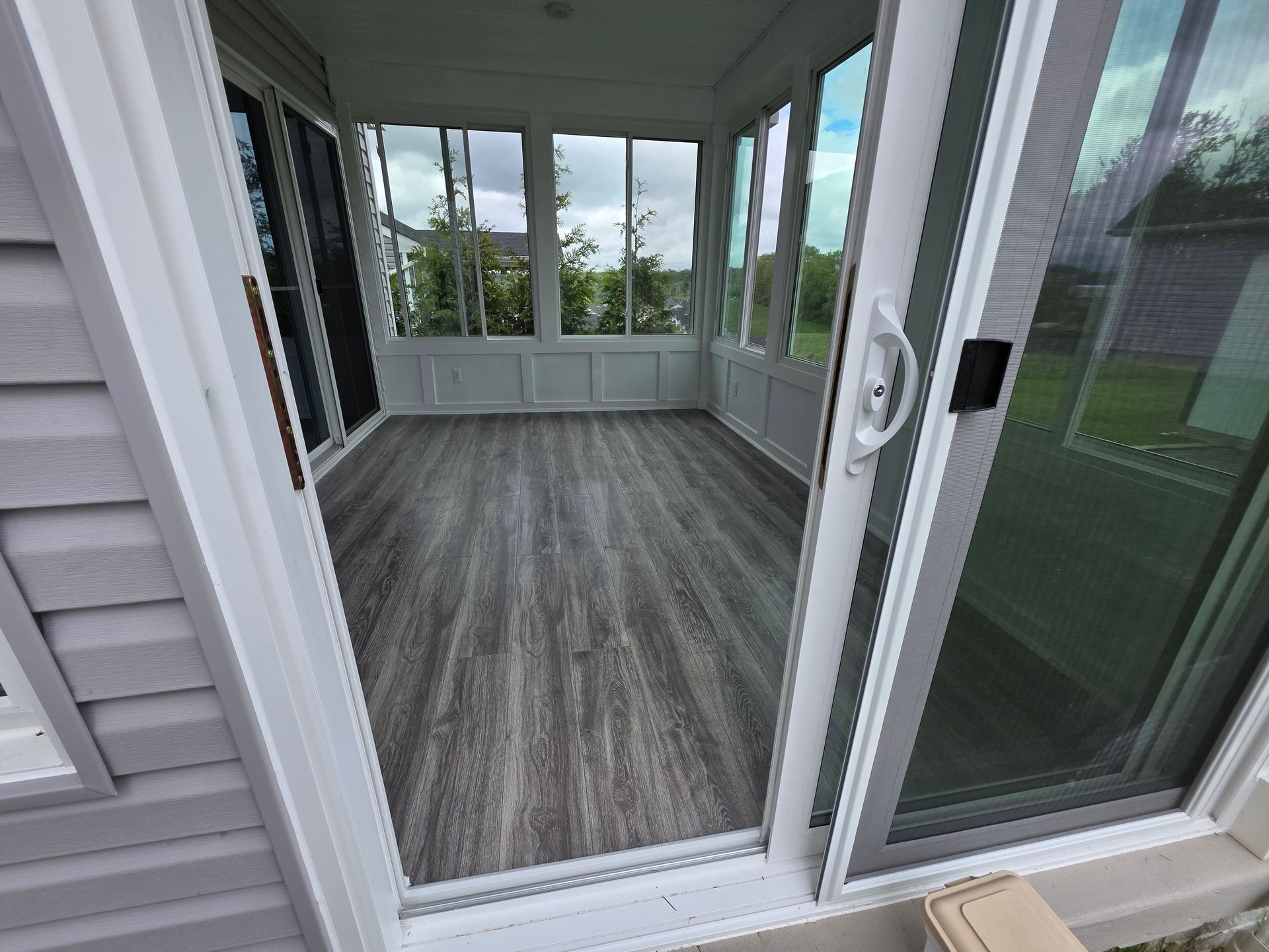 Sunroom with wood-look floor and large windows, viewed from an open sliding glass door.