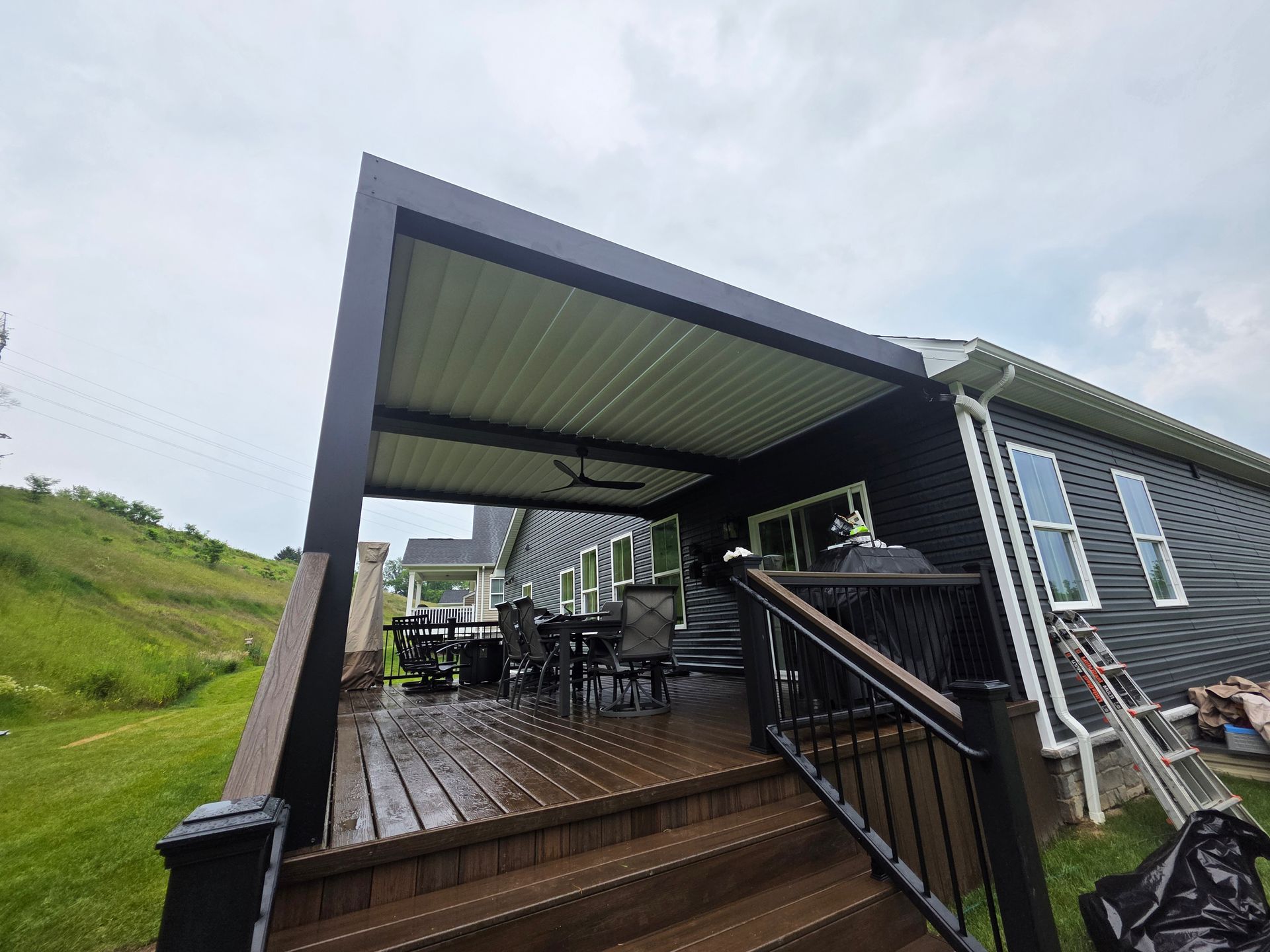 Covered outdoor deck with dining set, black siding, and overcast sky.