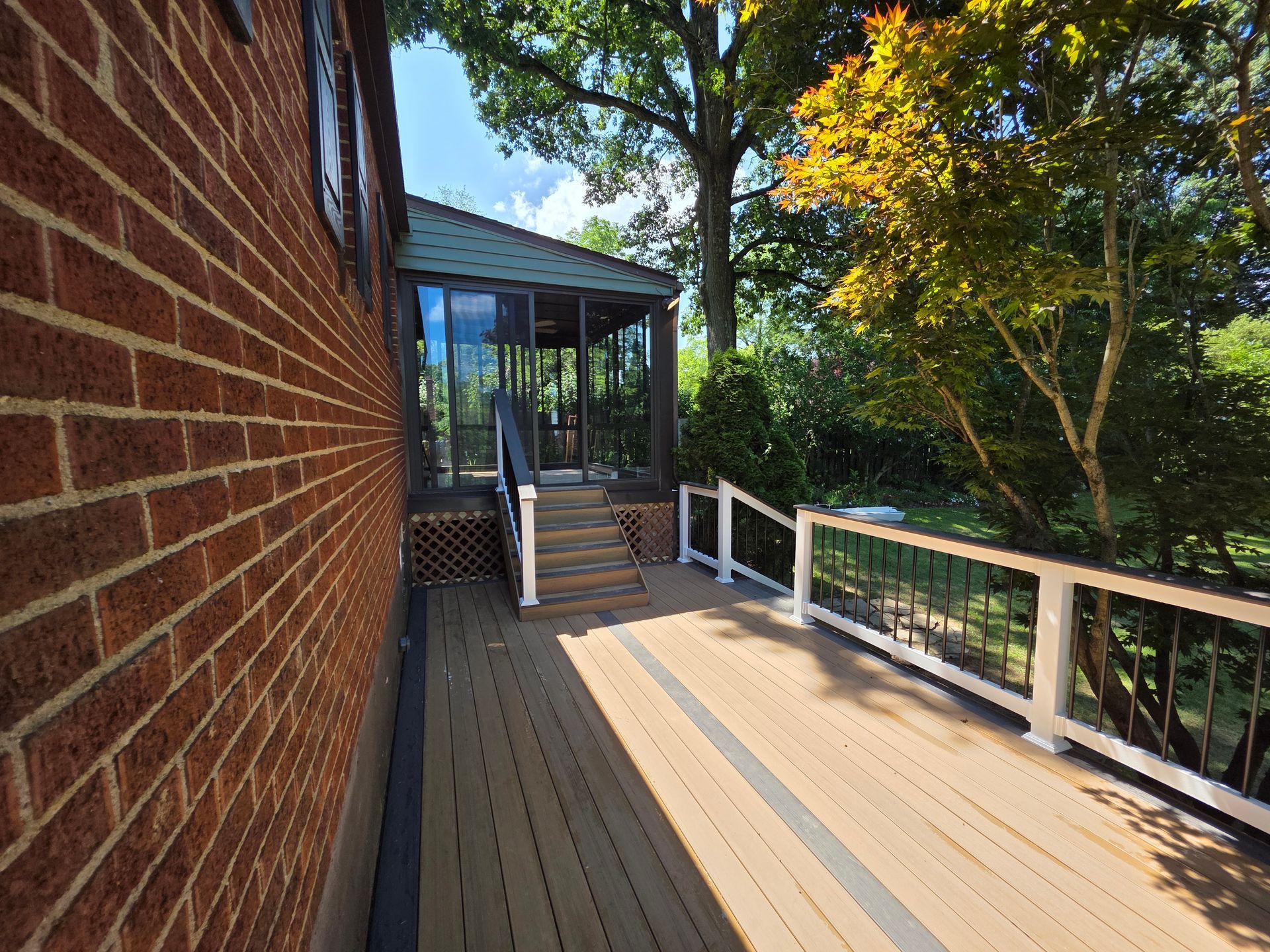 Brick house exterior with deck leading to a screened porch, surrounded by trees.