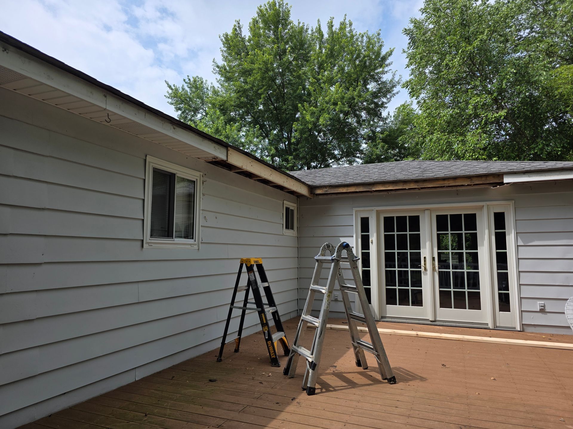 House exterior with two ladders; roof repair in progress. Cloudy sky, trees.