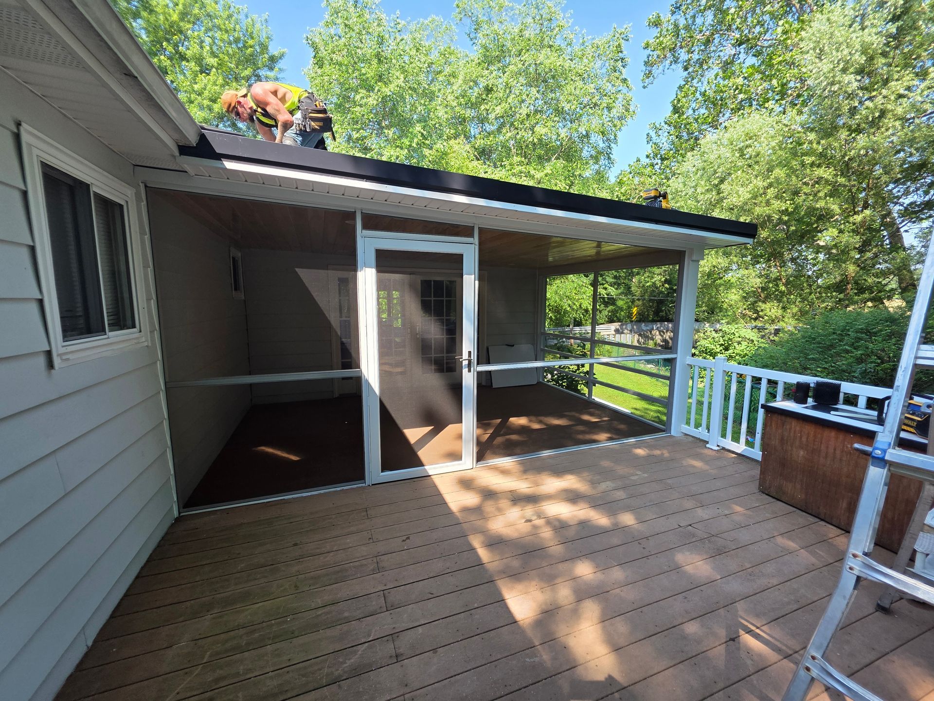 Screened porch attached to a house with a dark roof and a brown wooden deck.