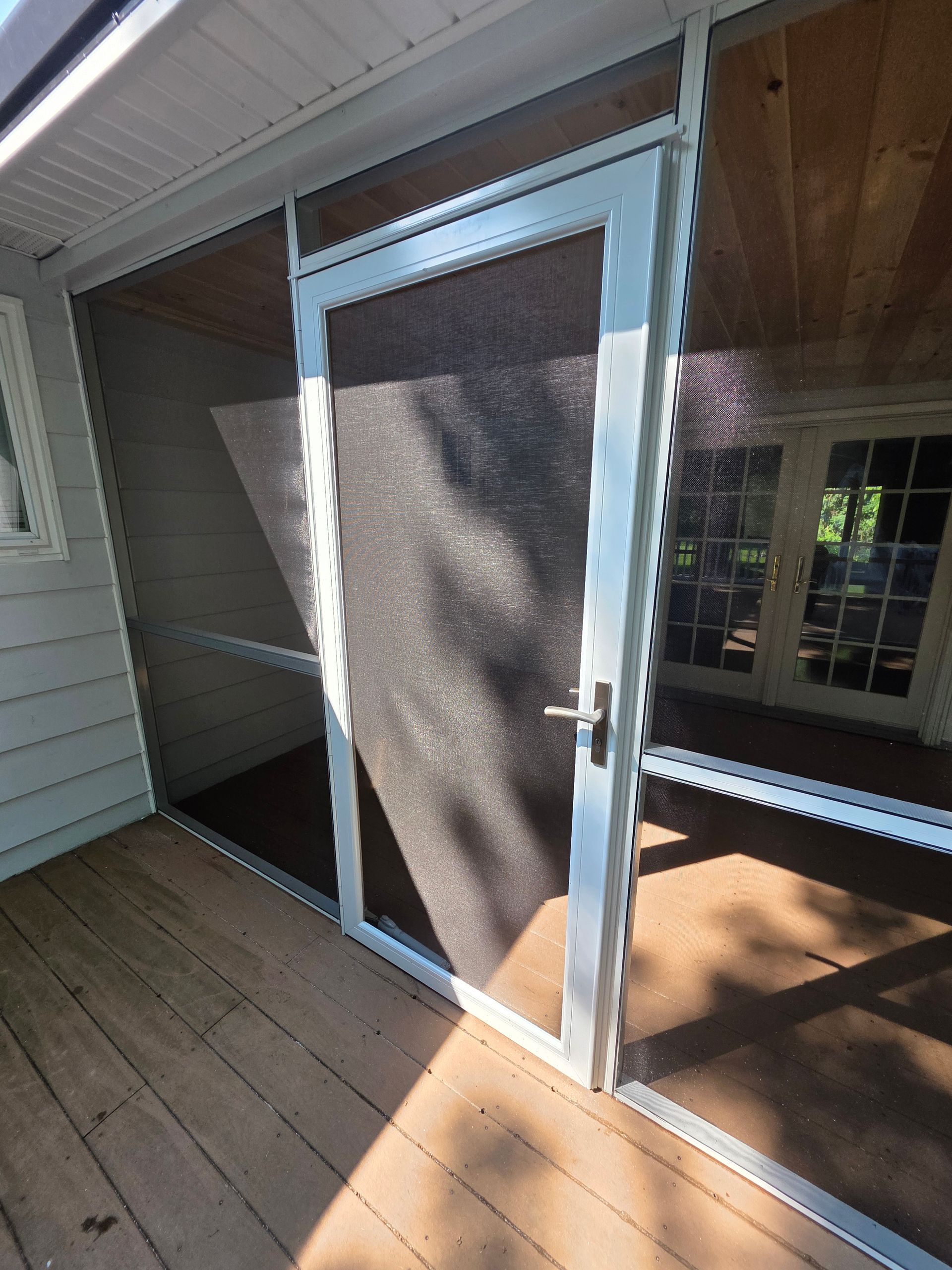 Screened porch door on wooden deck, leading to a home's interior. White trim, black screen.