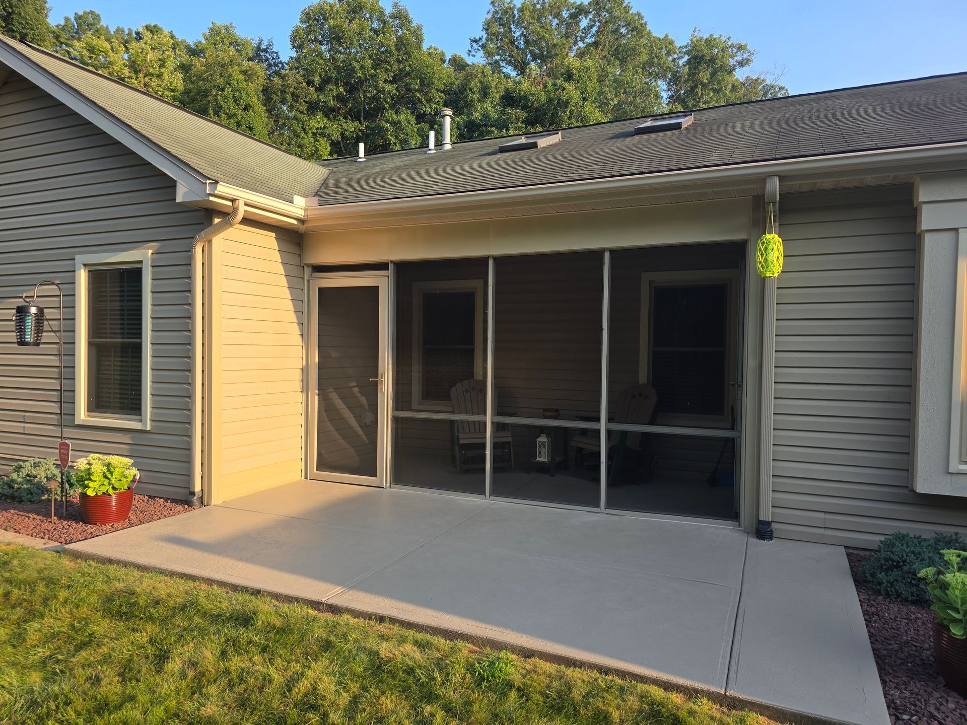 A screened-in patio with concrete flooring, attached to a house with beige siding, and green lawn.