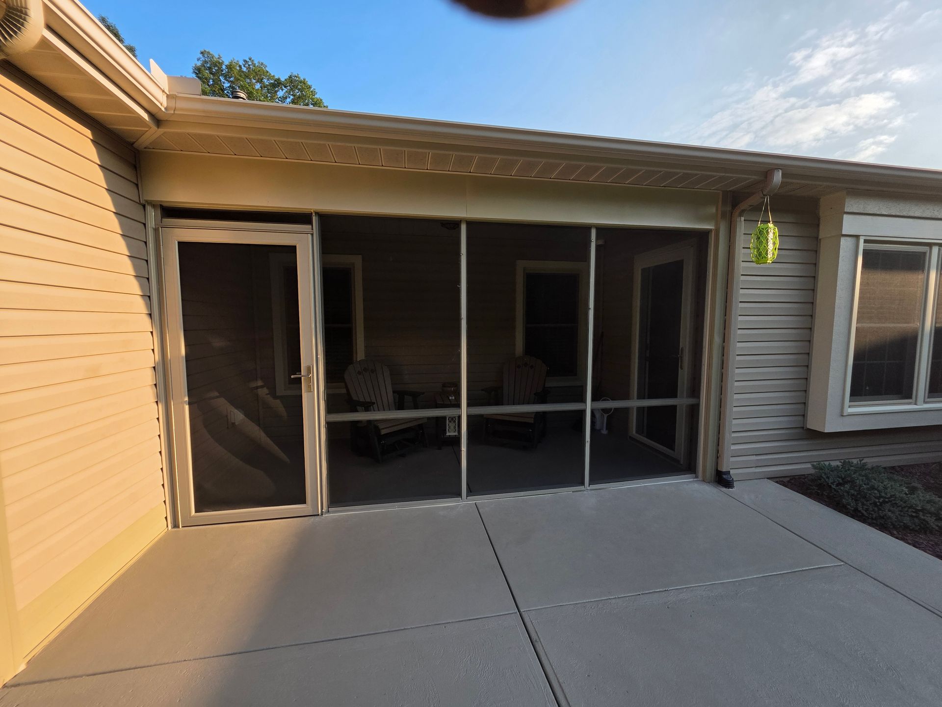 Screened patio with concrete floor, tan siding, and chairs visible inside.