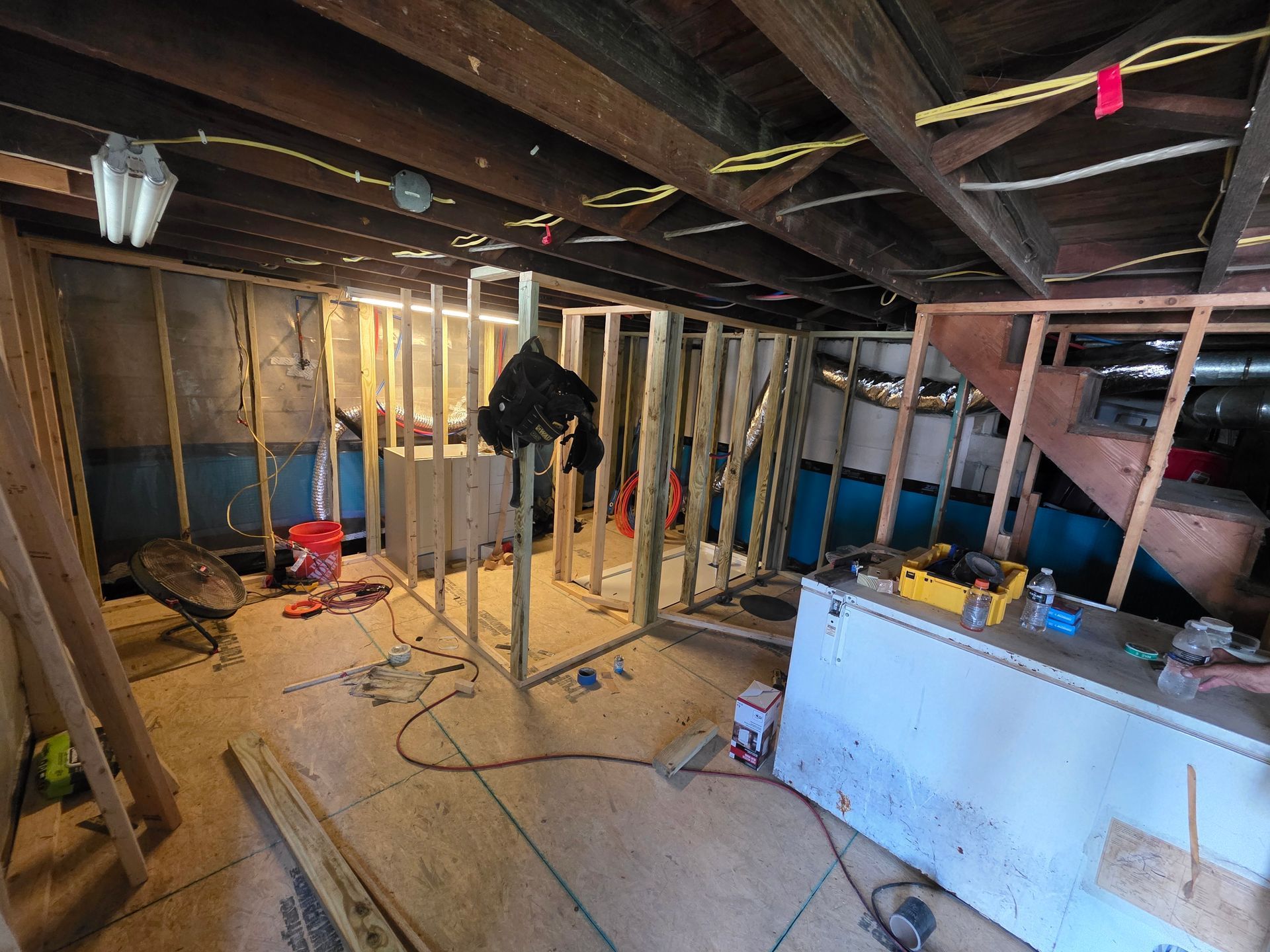 Basement under construction: wooden framing, exposed beams, tools, and a white cabinet.
