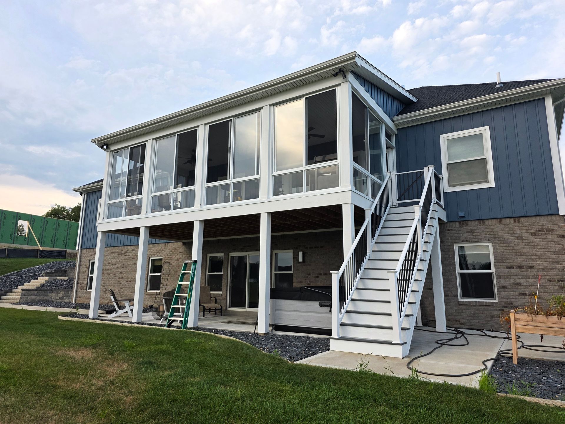 Two-story house with screened porch and stairs, blue siding, brick base, and lush green lawn.
