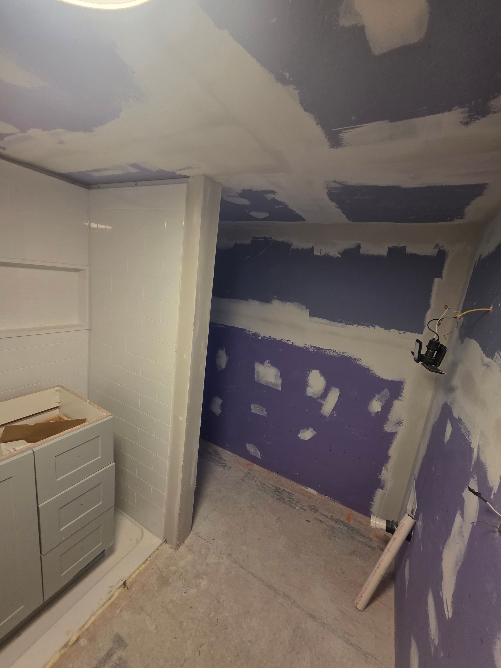 Bathroom under construction; purple drywall, white shower stall, gray cabinet, bare floor.