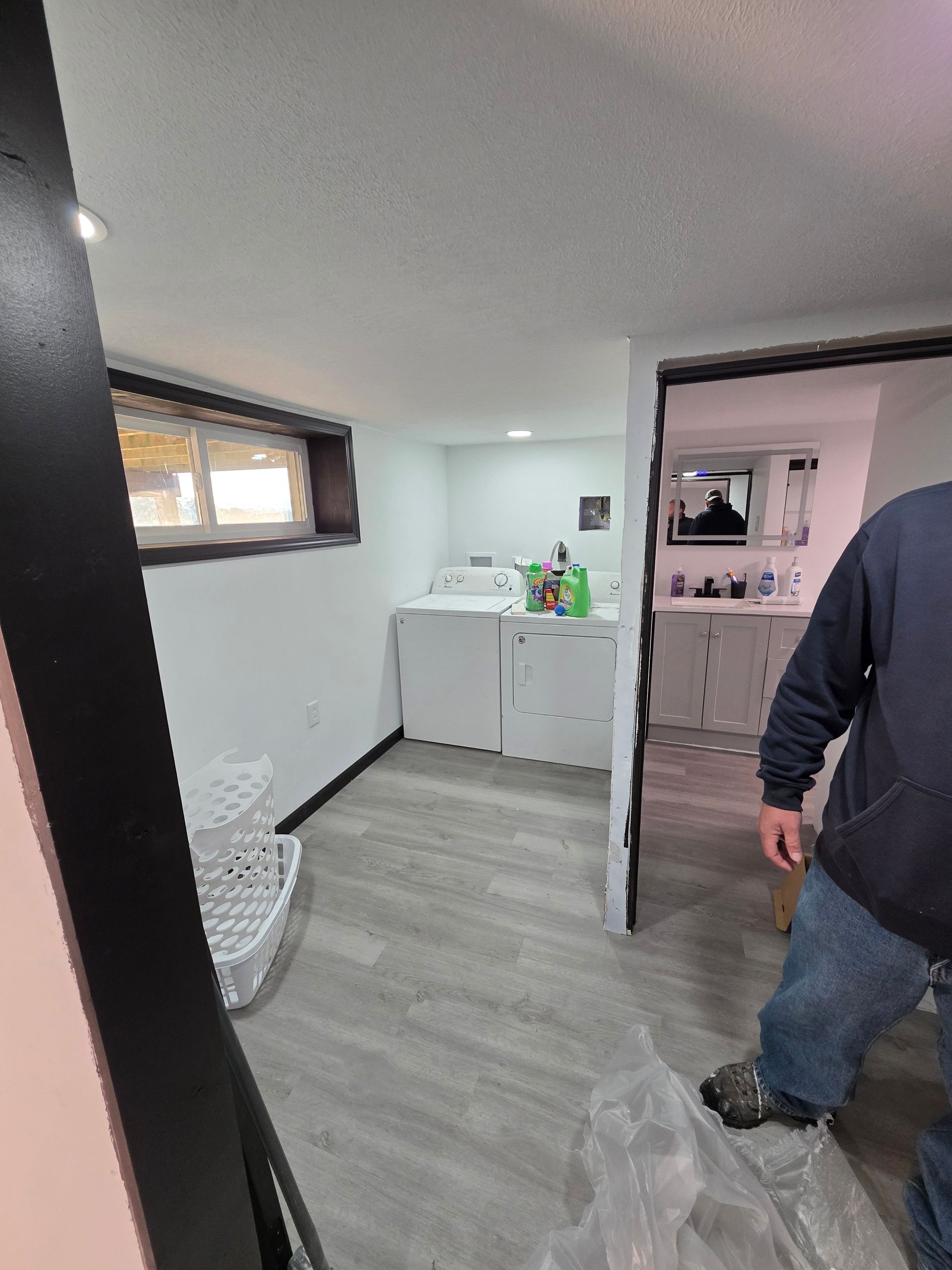 Laundry room with washer, dryer, and doorway leading to a bathroom. A person stands nearby.