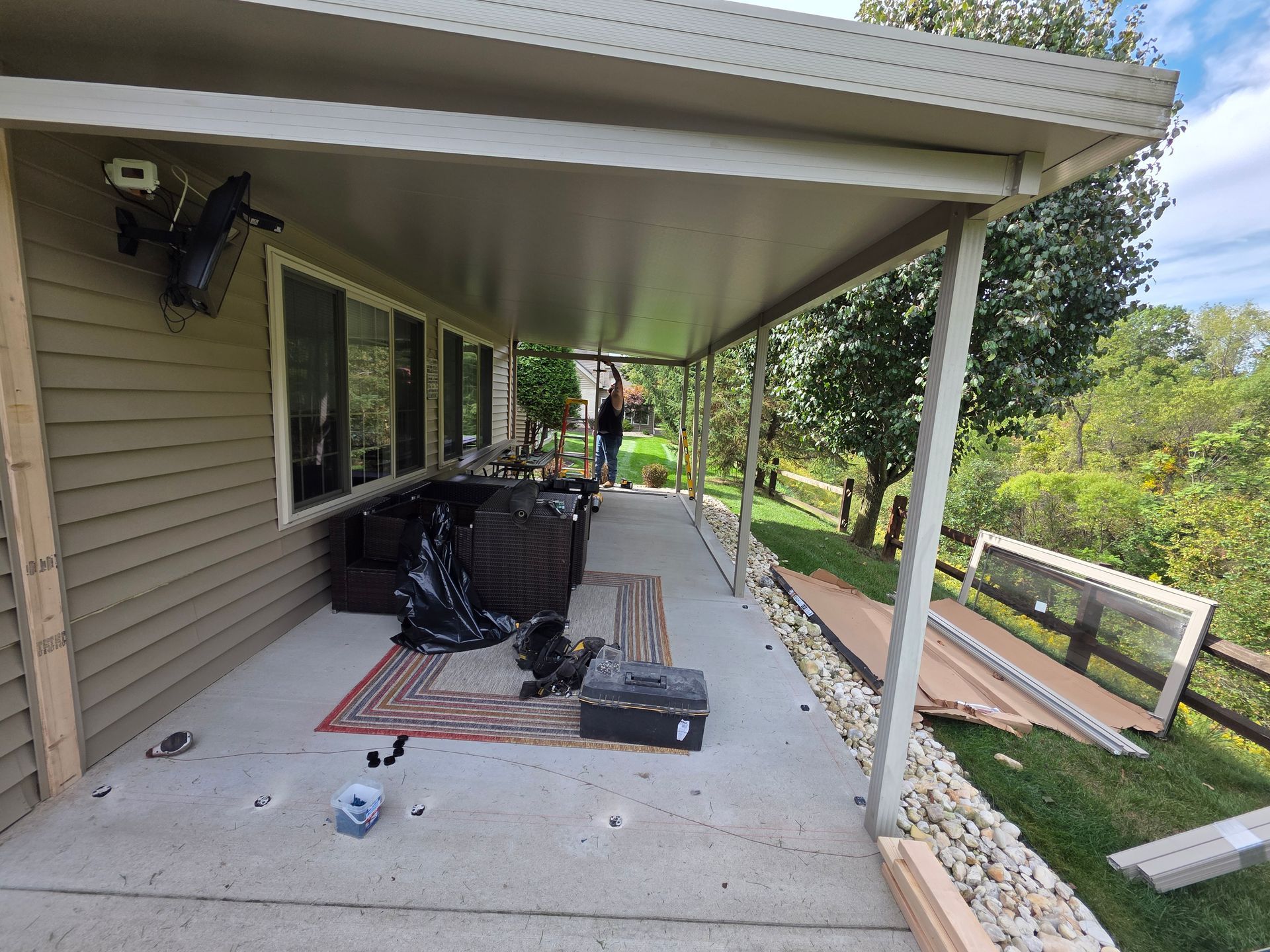 Covered patio with a person, furniture, debris, and a grassy area.