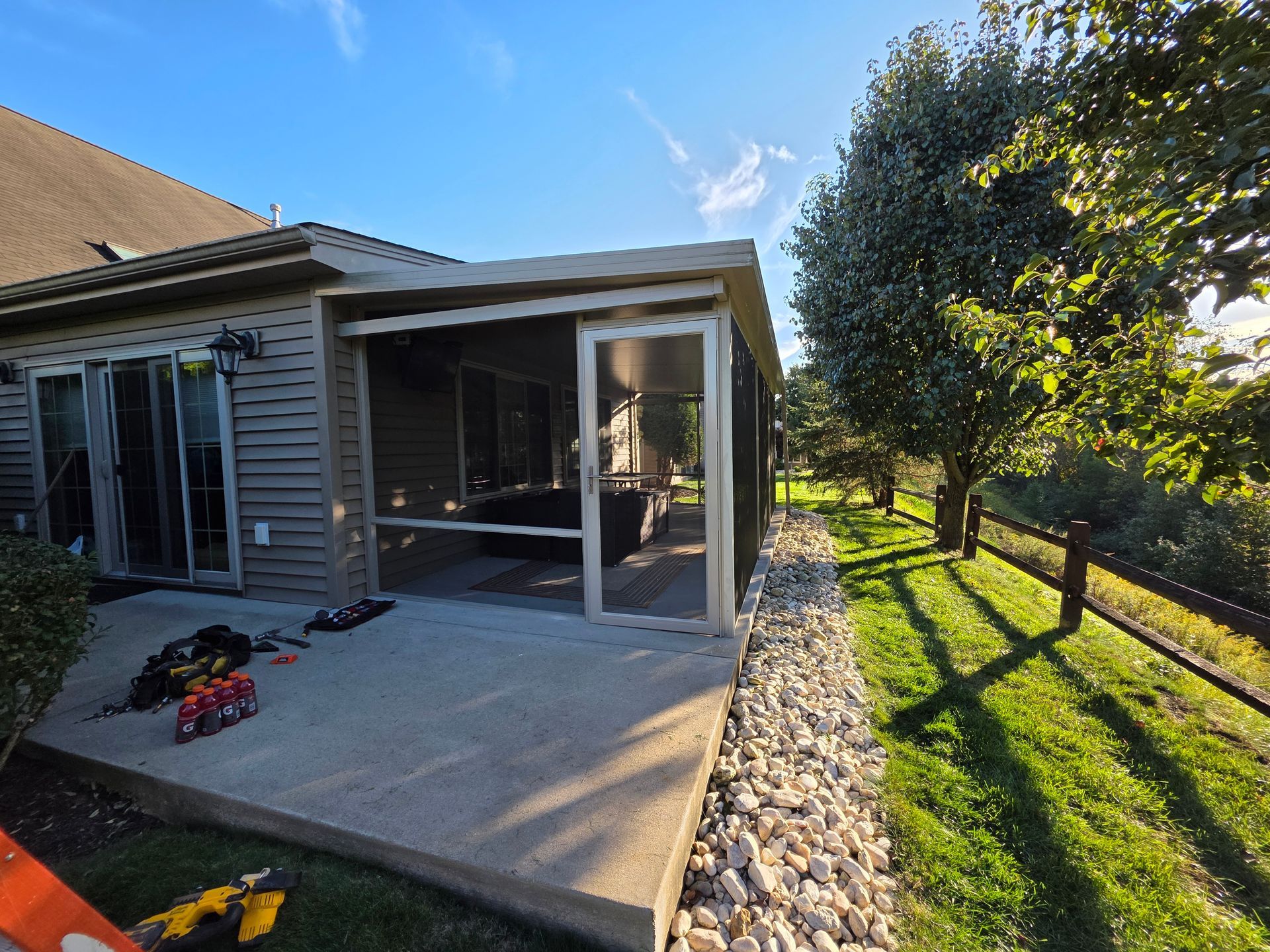 Screened patio attached to a house with sliding glass doors, concrete patio, and stone landscaping.