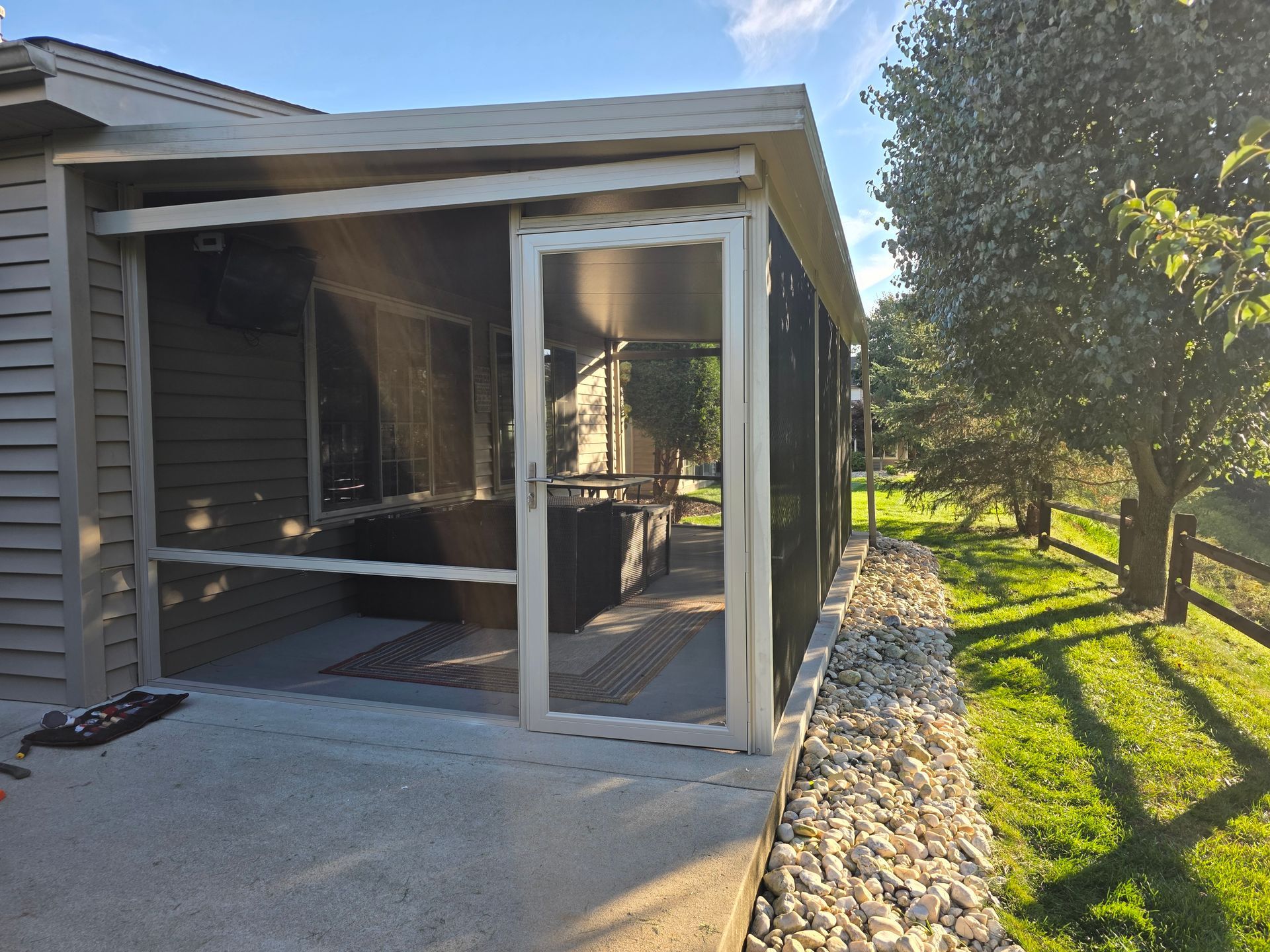 Screened-in porch on a concrete patio with a view of a grassy yard, and trees.