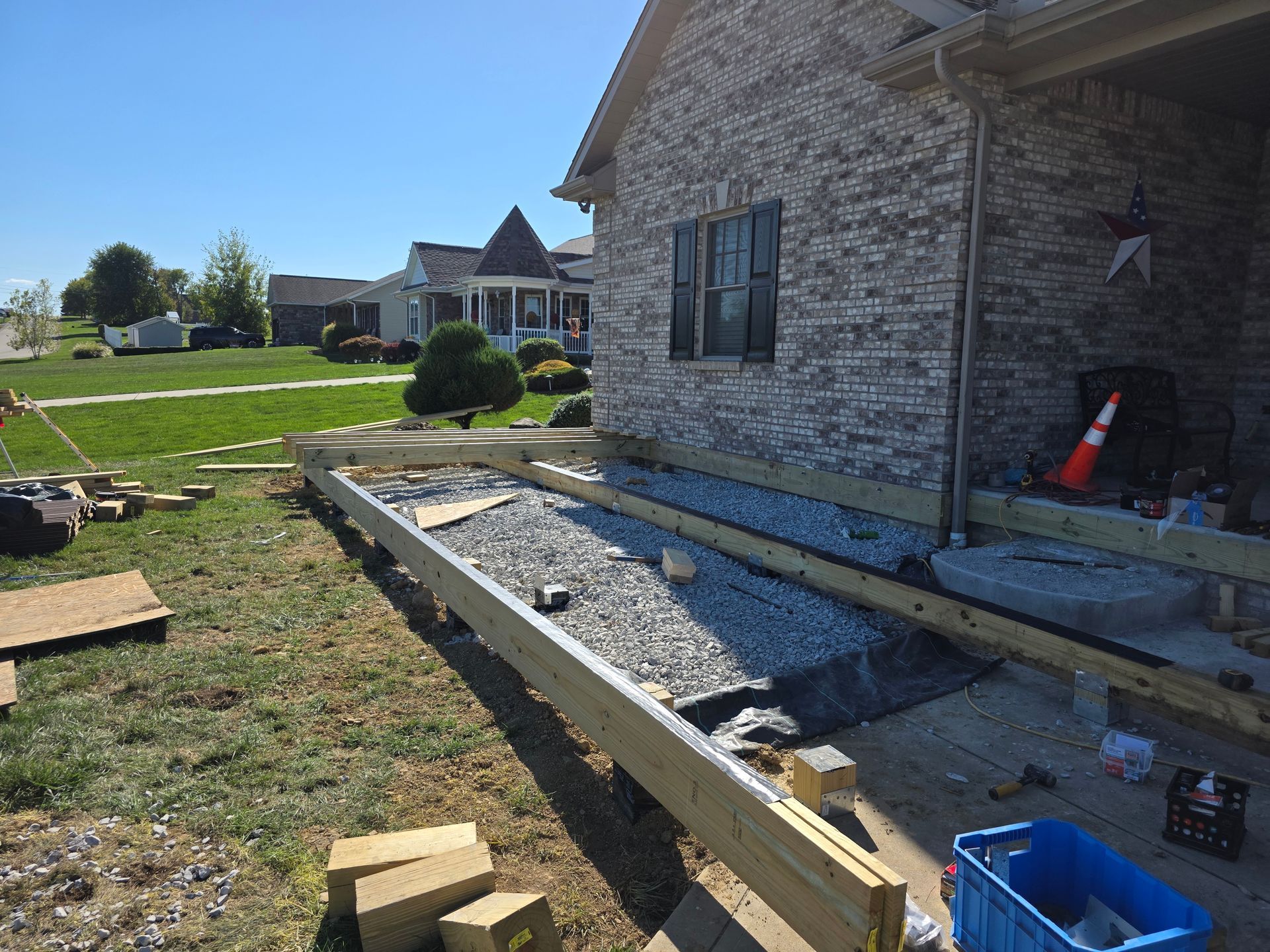 Construction of a wooden deck and a gravel-filled area next to a brick house.