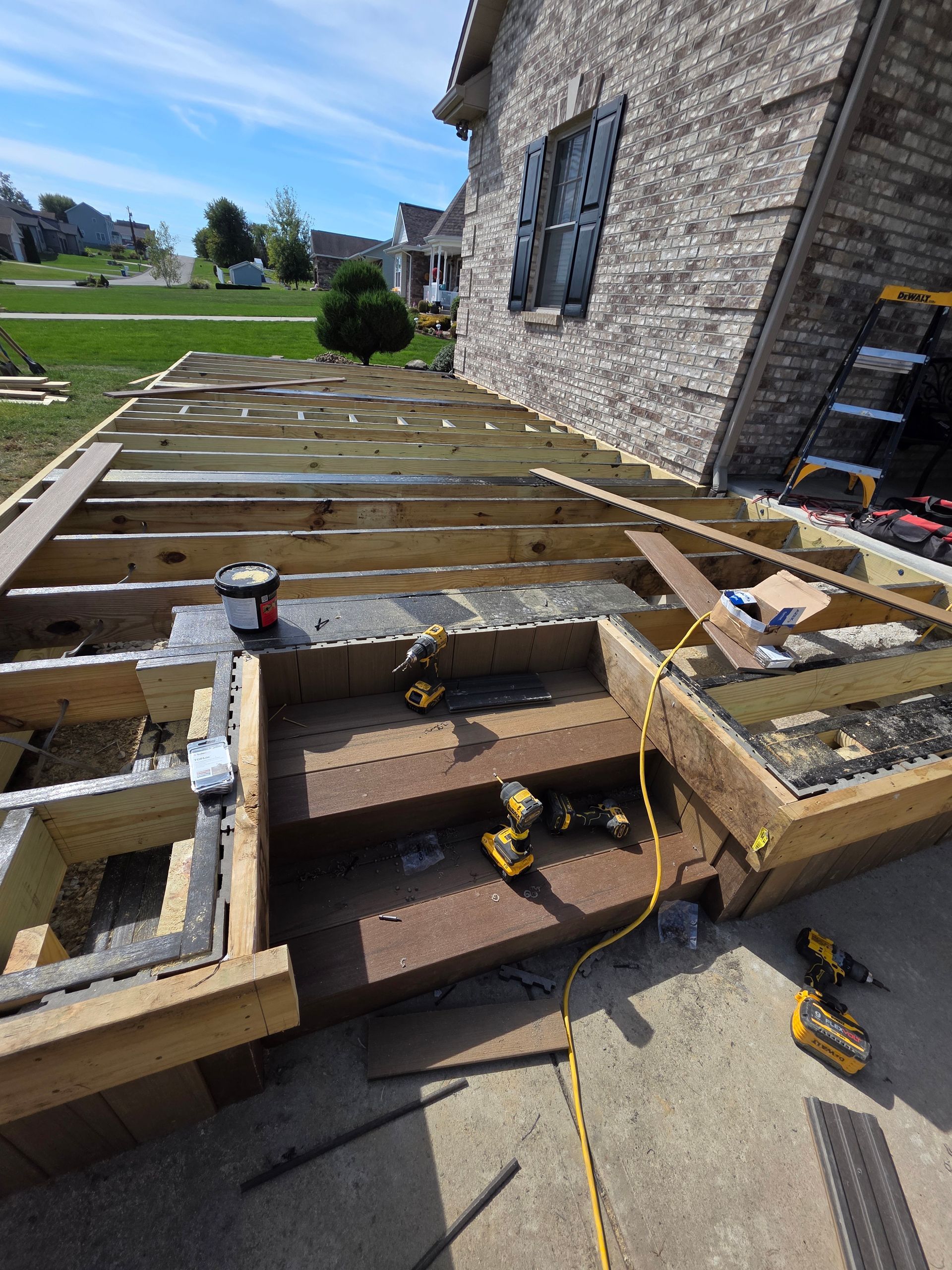 Deck construction in progress near a brick house; wooden frame and stairs visible.