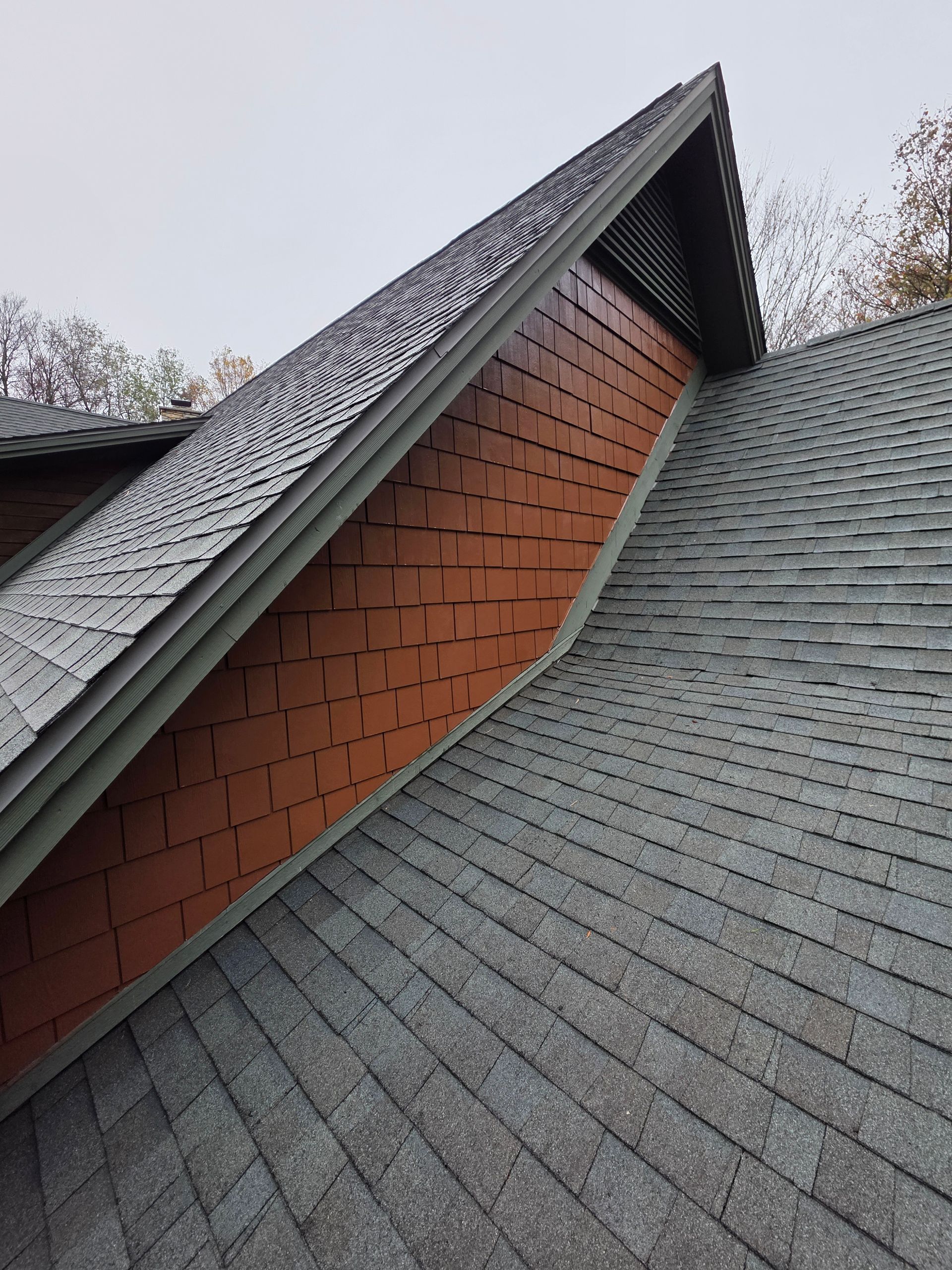 Angled view of a house roof with brown siding between gray shingle sections.