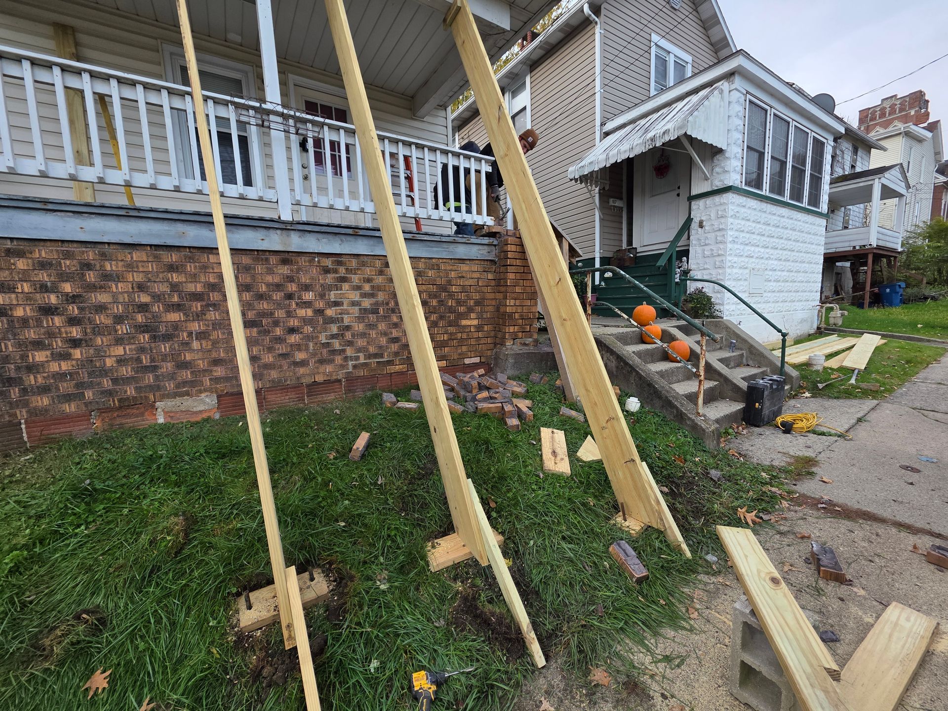 Three wooden supports leaning on a house; pumpkins on steps.