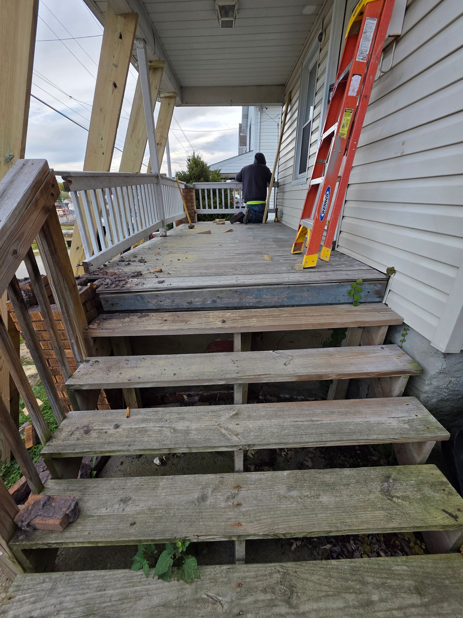 Wooden porch stairs leading to a dilapidated porch with a ladder leaning against the building.