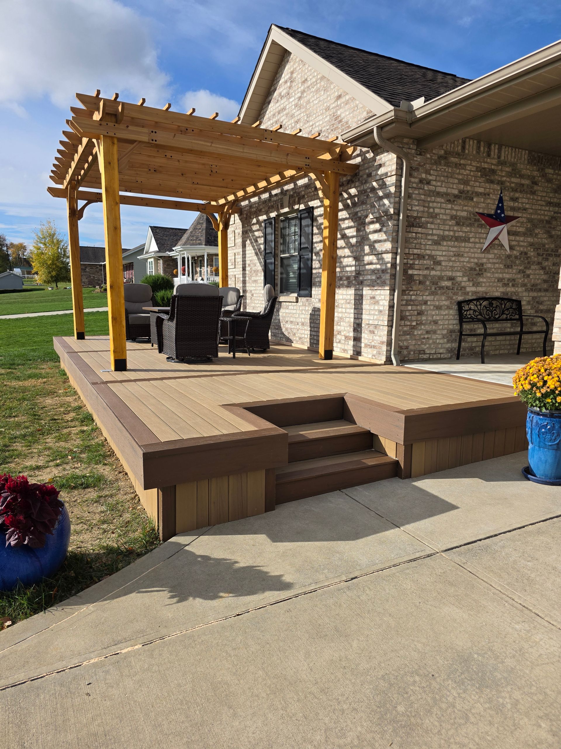 Wooden pergola over a composite deck with built-in steps, beside a brick house.
