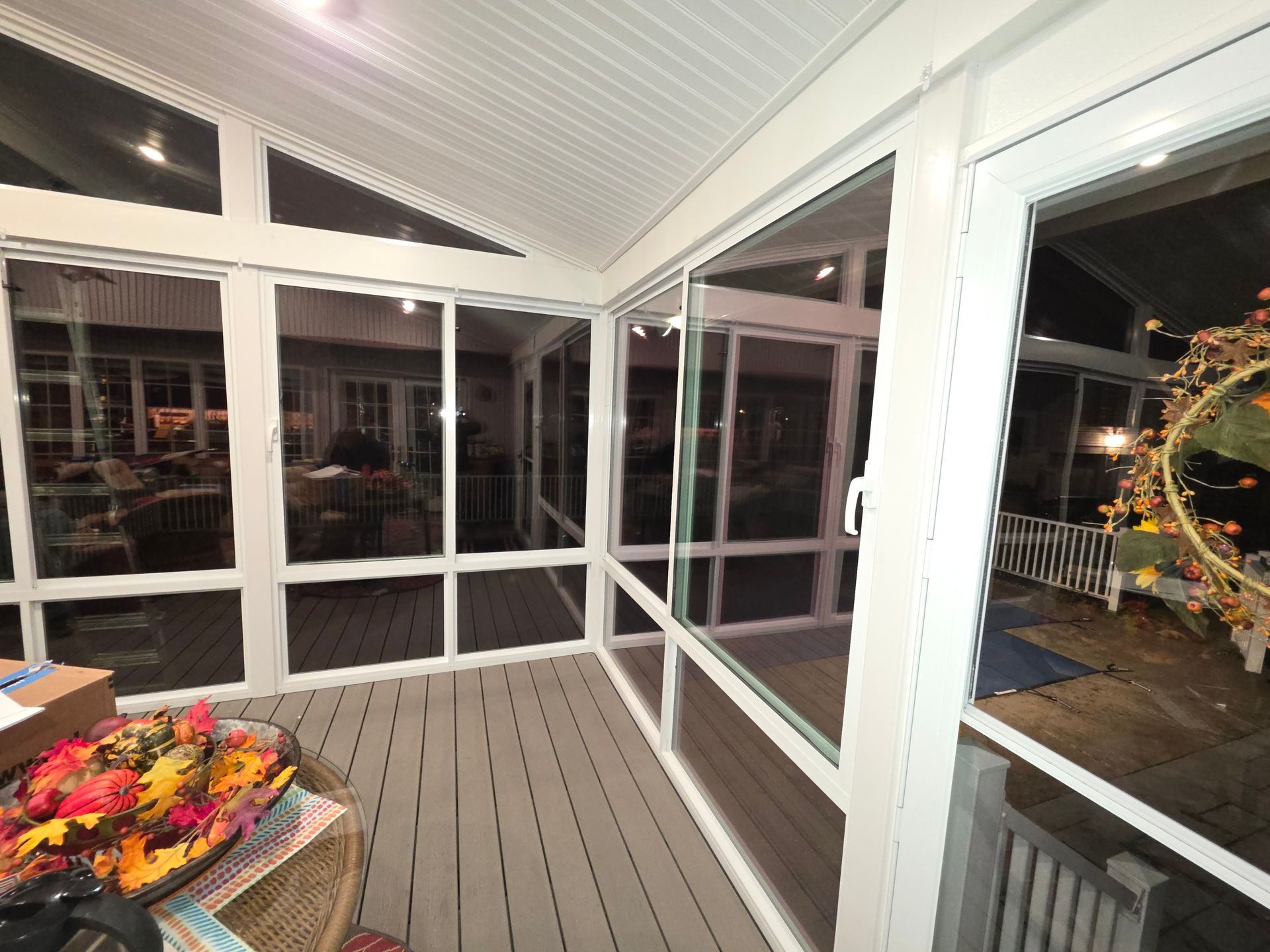 Enclosed porch with white trim, gray floor, glass windows, and a fall wreath visible outside.