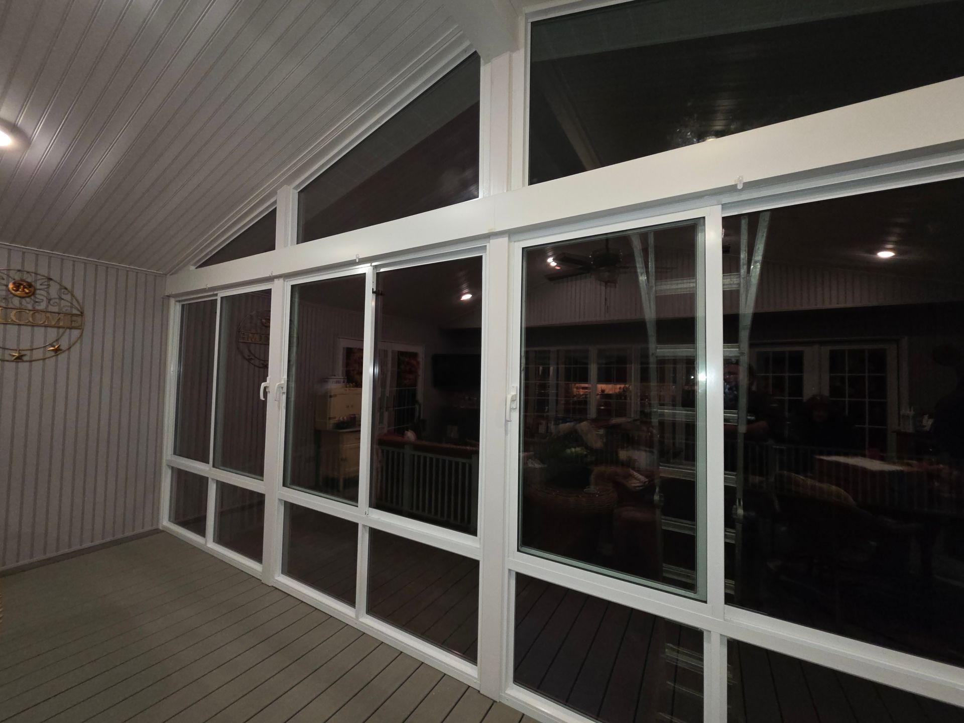 White-framed screened porch with large windows and a sloped ceiling, overlooking a dimly lit interior.