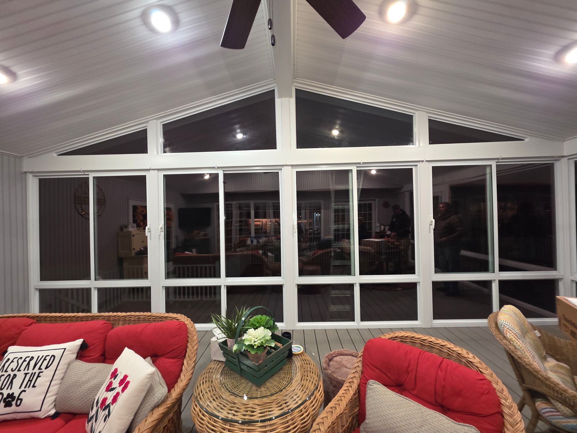 Sunroom with red wicker furniture, windows, and potted plants, overlooking a home's interior.