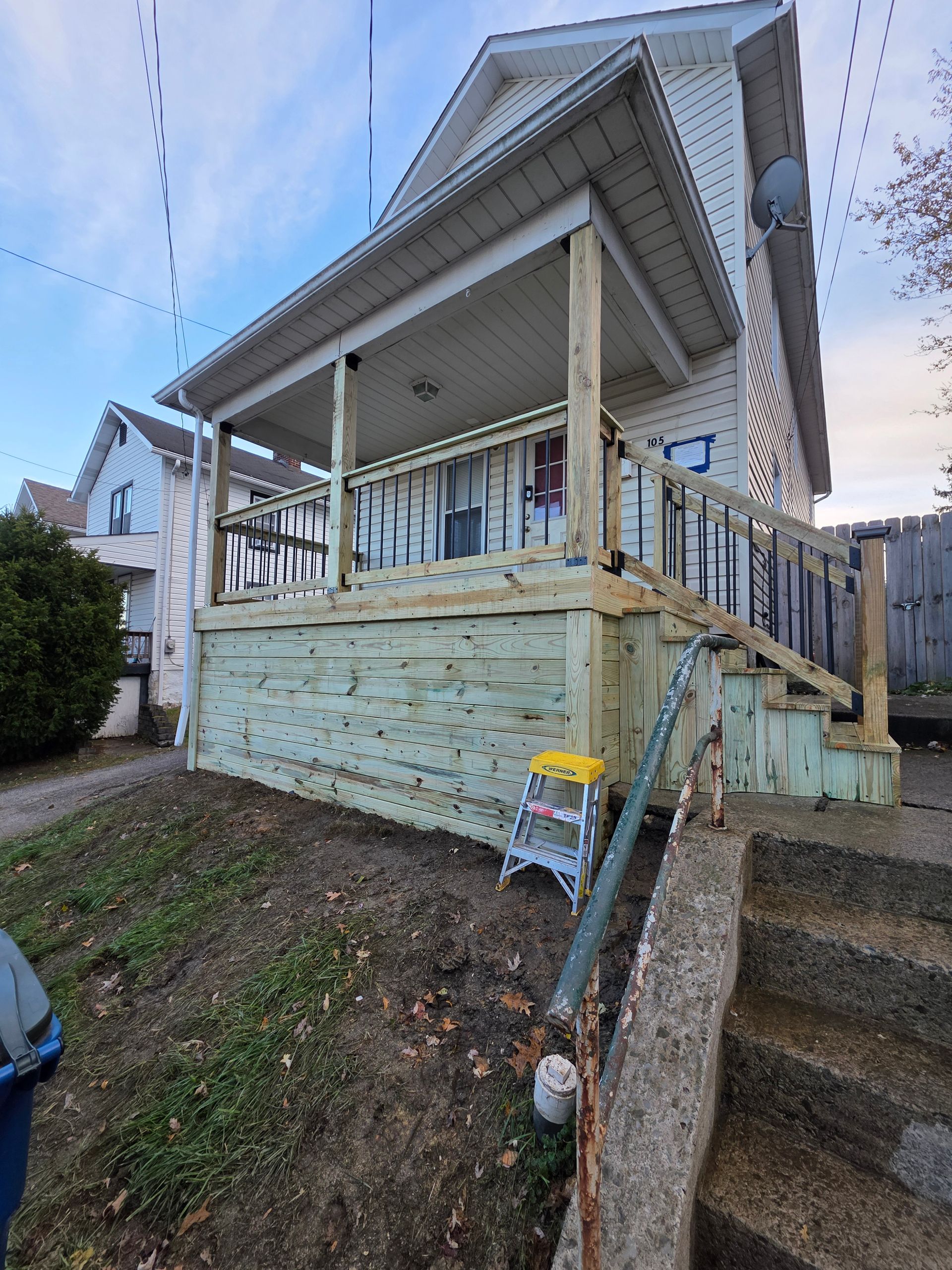 Two-story house with a wooden porch and steps leading up from the lawn.