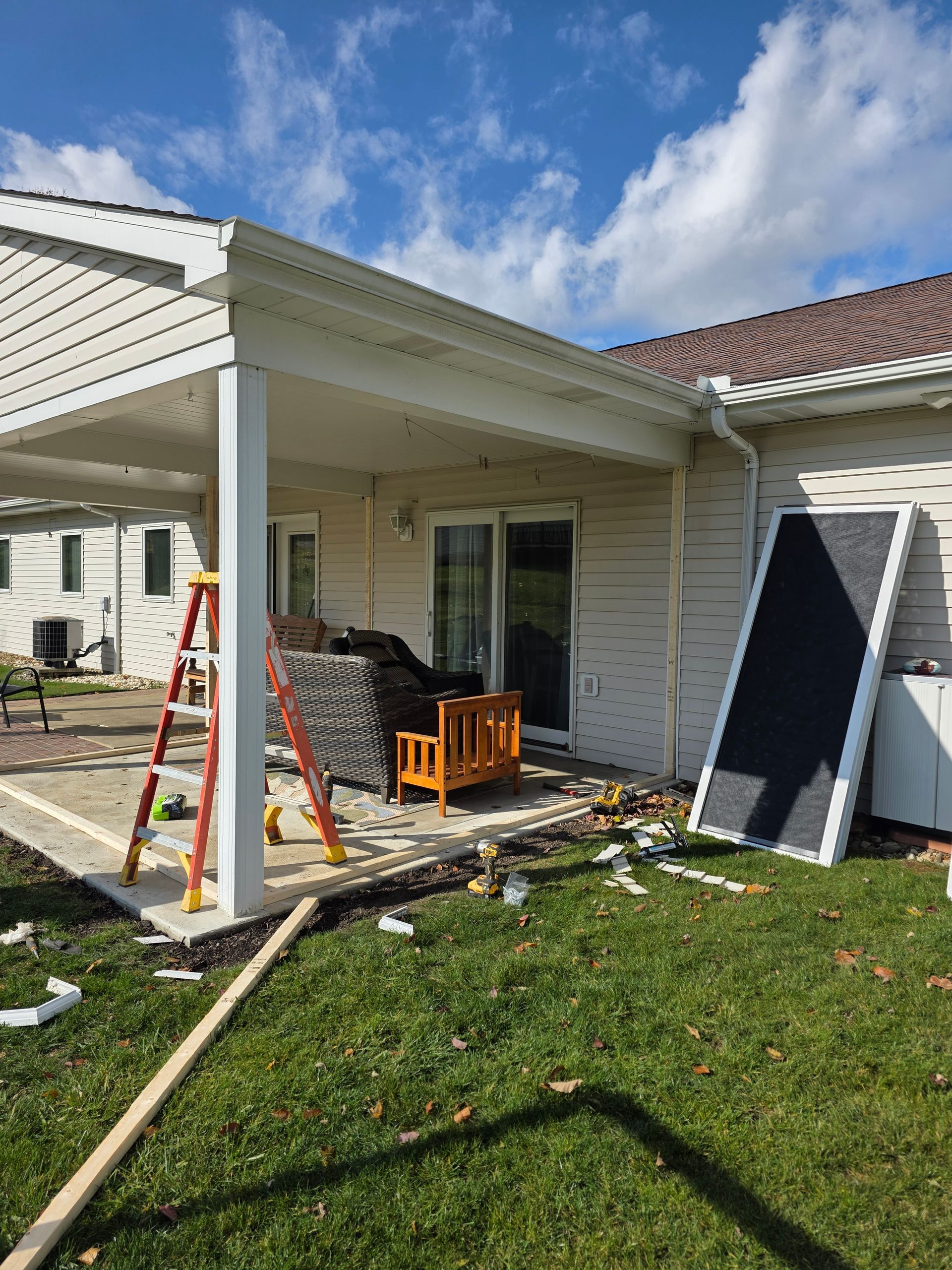 Backyard with patio and construction materials, including a ladder and a large panel, under a sunny sky.