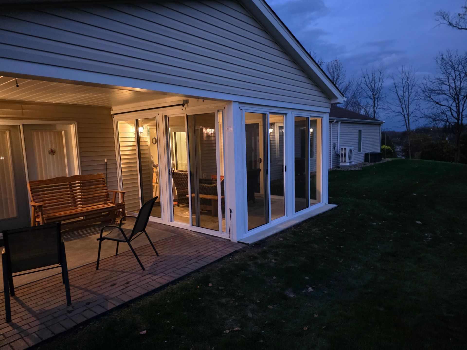 A home's patio with a swing, chairs, and a glass-enclosed sunroom at dusk.
