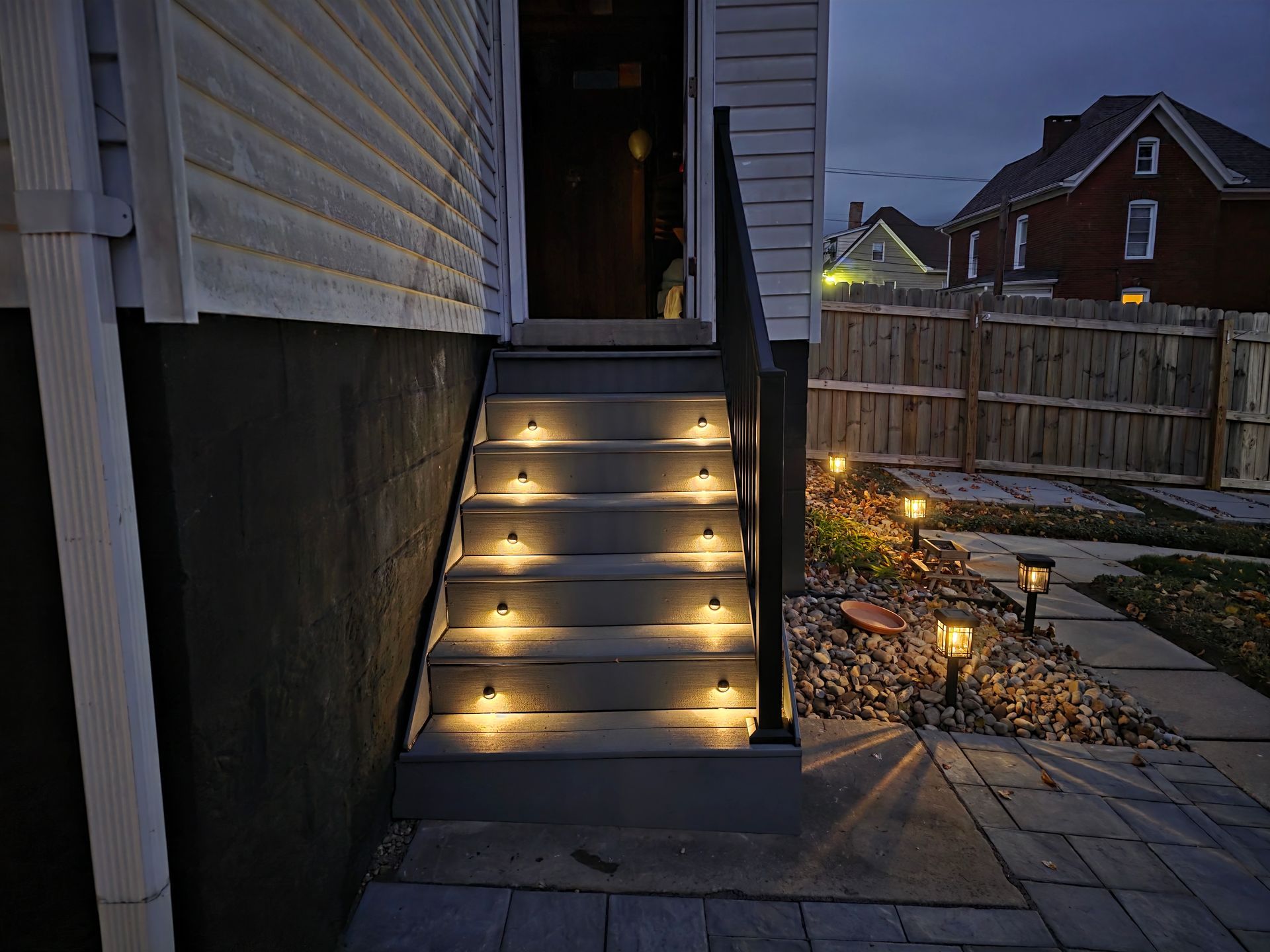 Exterior stairs with integrated lights leading to a door, illuminated at dusk. Pathway lights in garden.